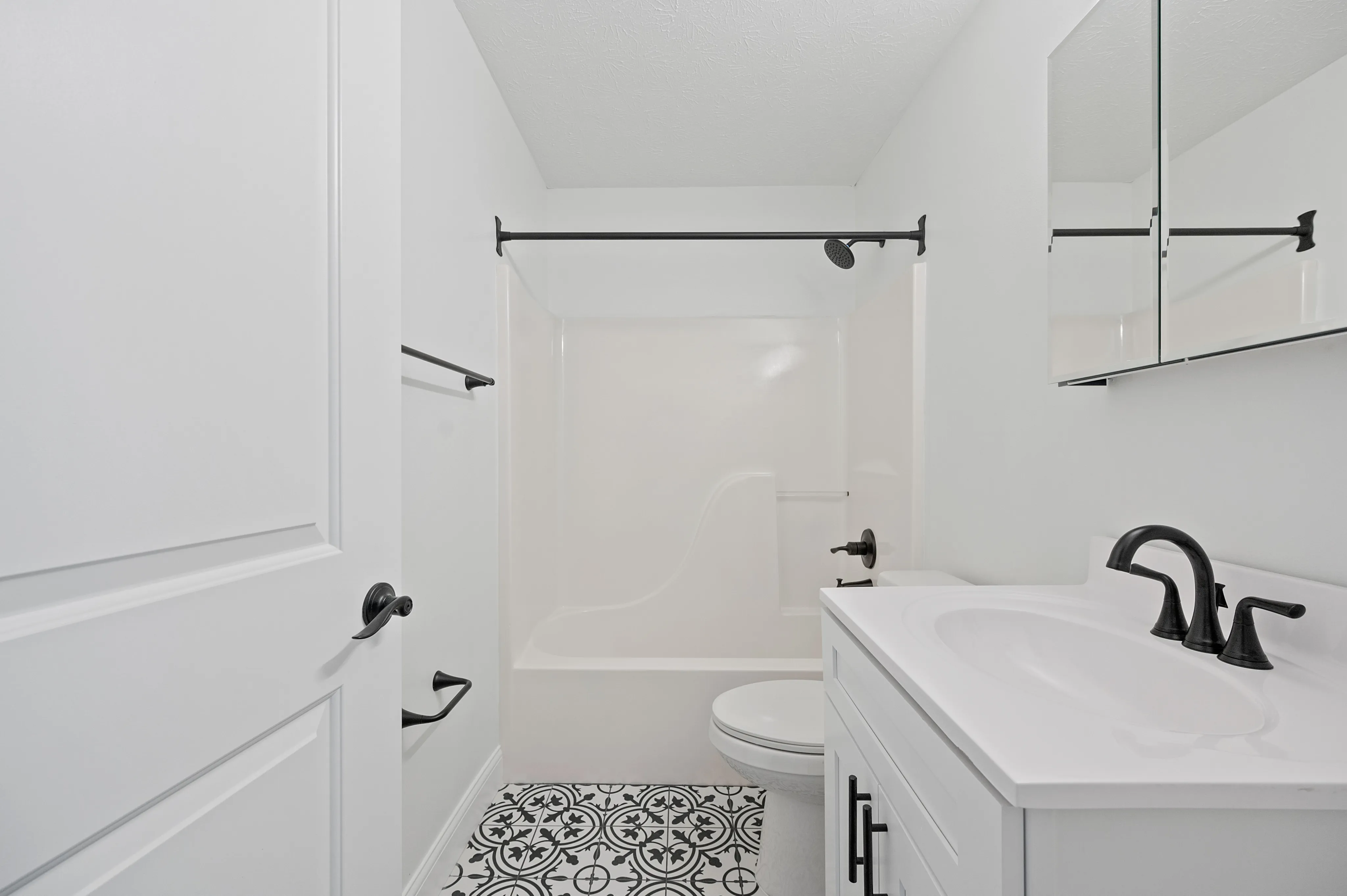 Modern bathroom featuring a sleek white vanity, black fixtures, and decorative tile flooring.