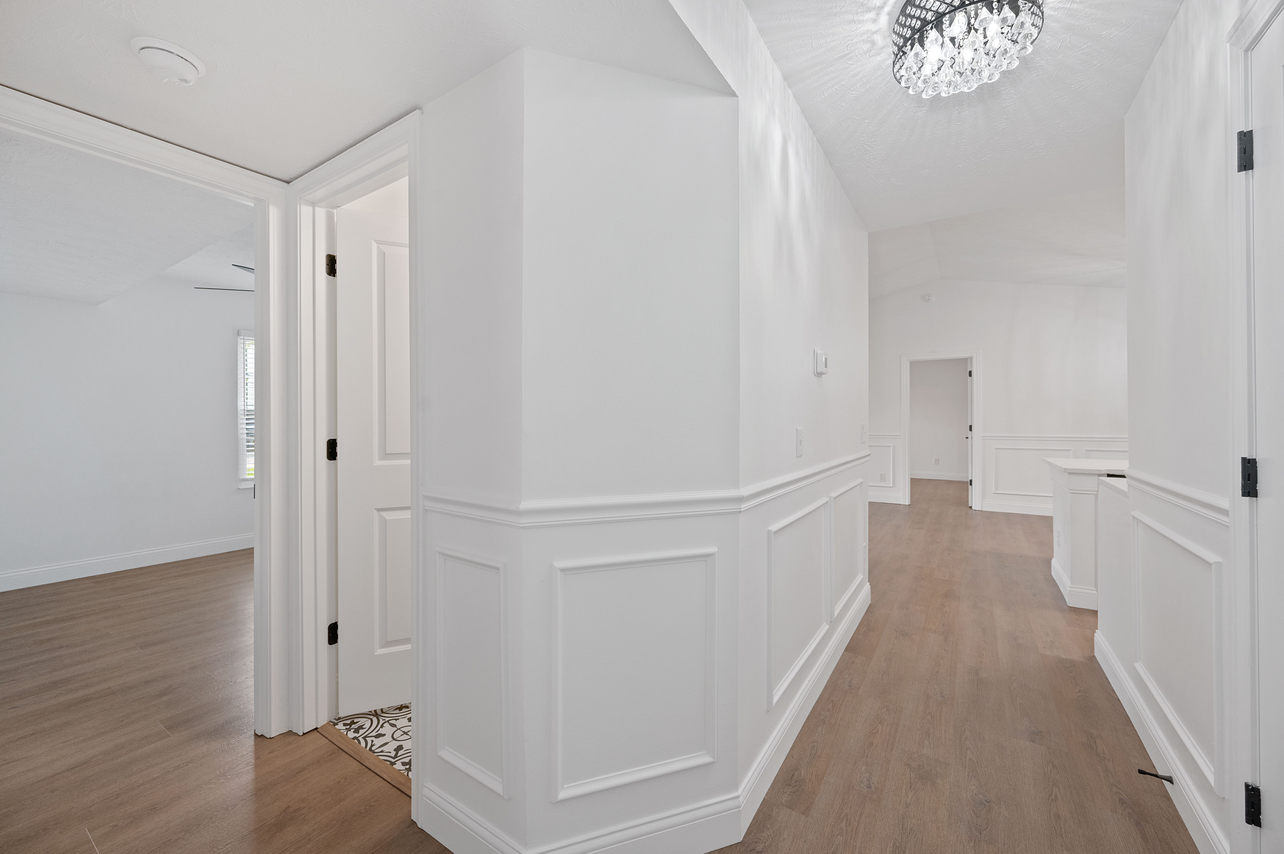 Bright hallway with elegant wainscoting and wooden flooring, leading to multiple rooms.