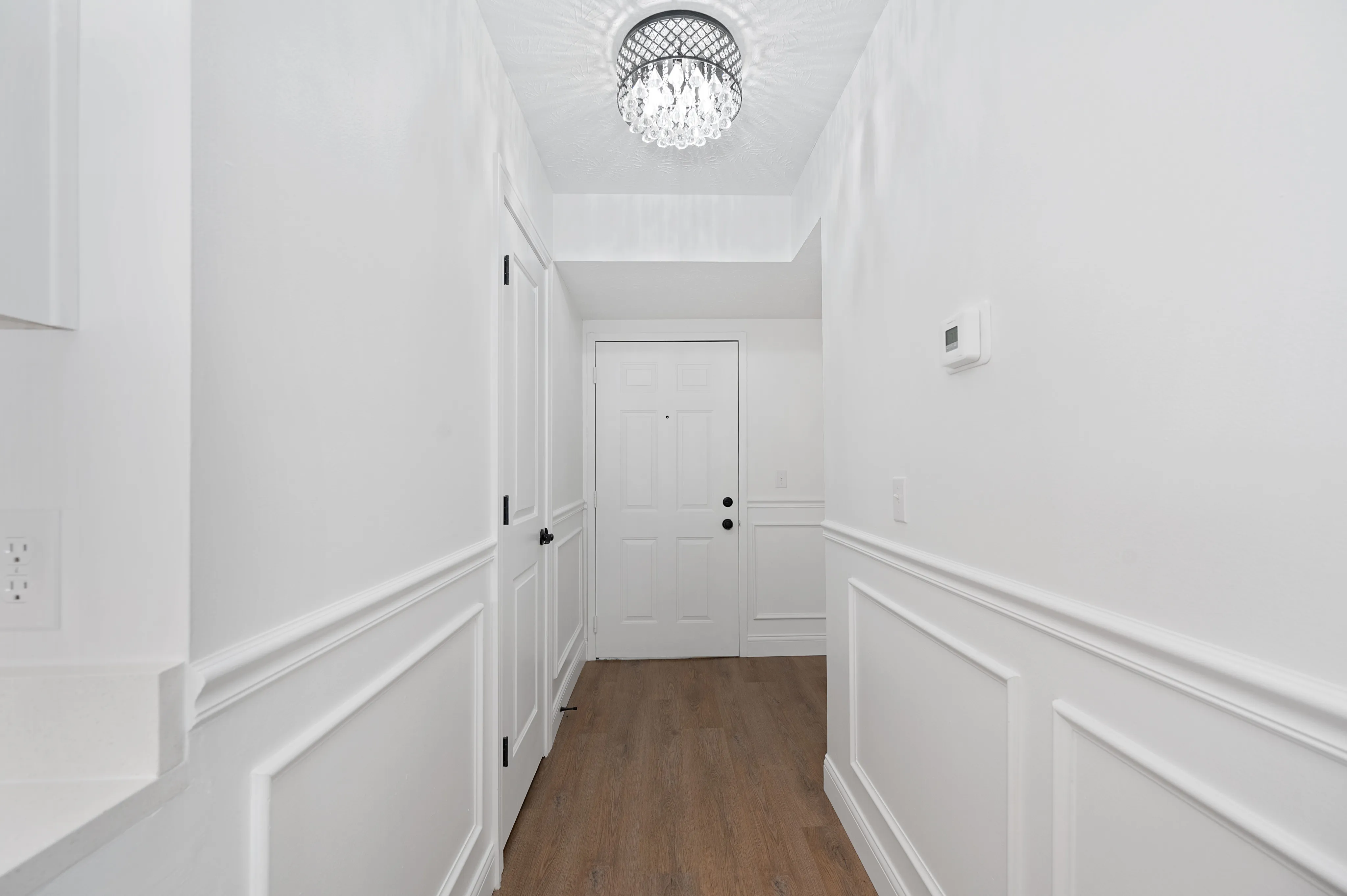 Bright entryway with modern chandelier and wood flooring.