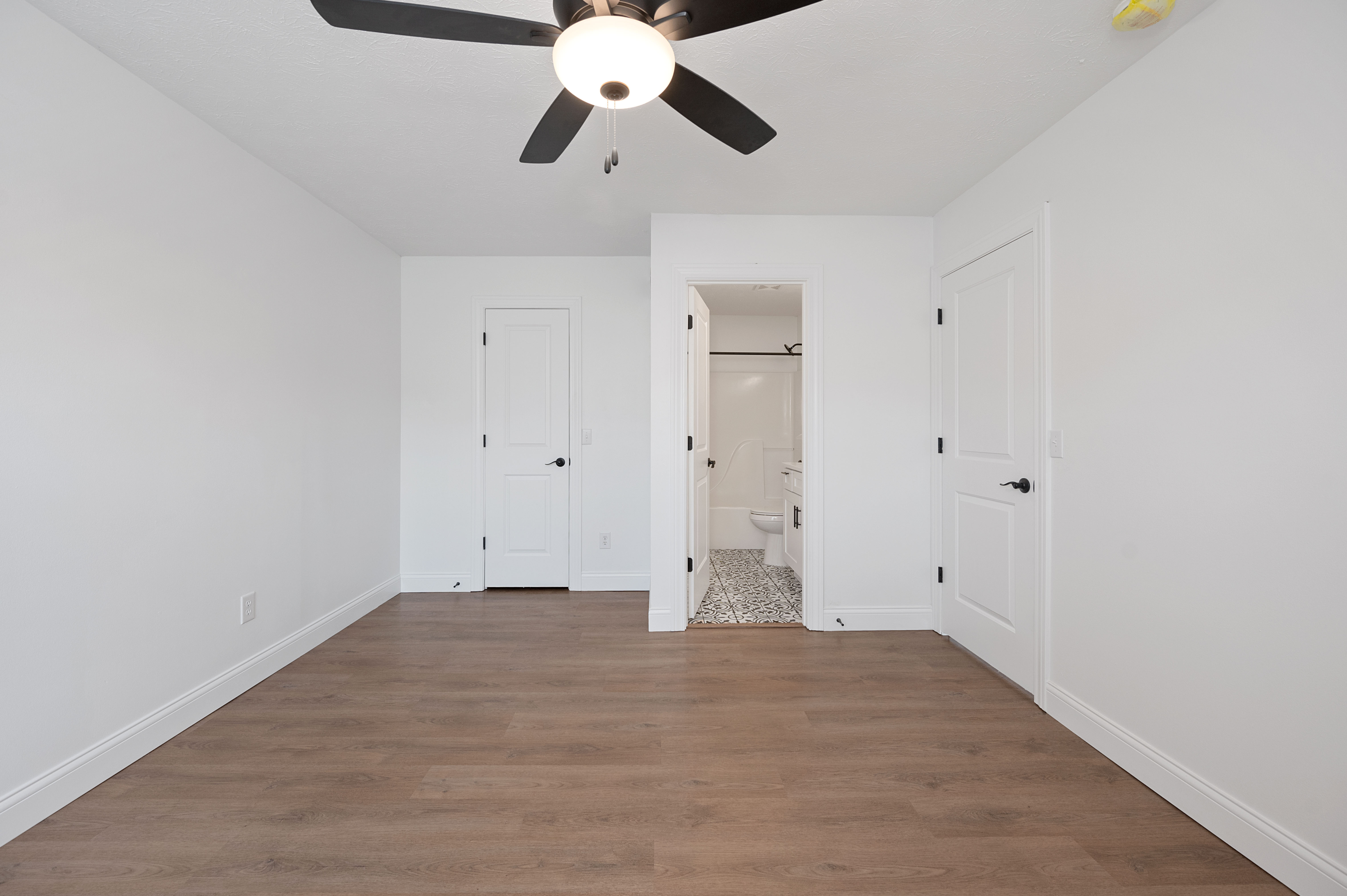 Bright, airy bedroom with light wood flooring and ceiling fan, leading to an ensuite bathroom.