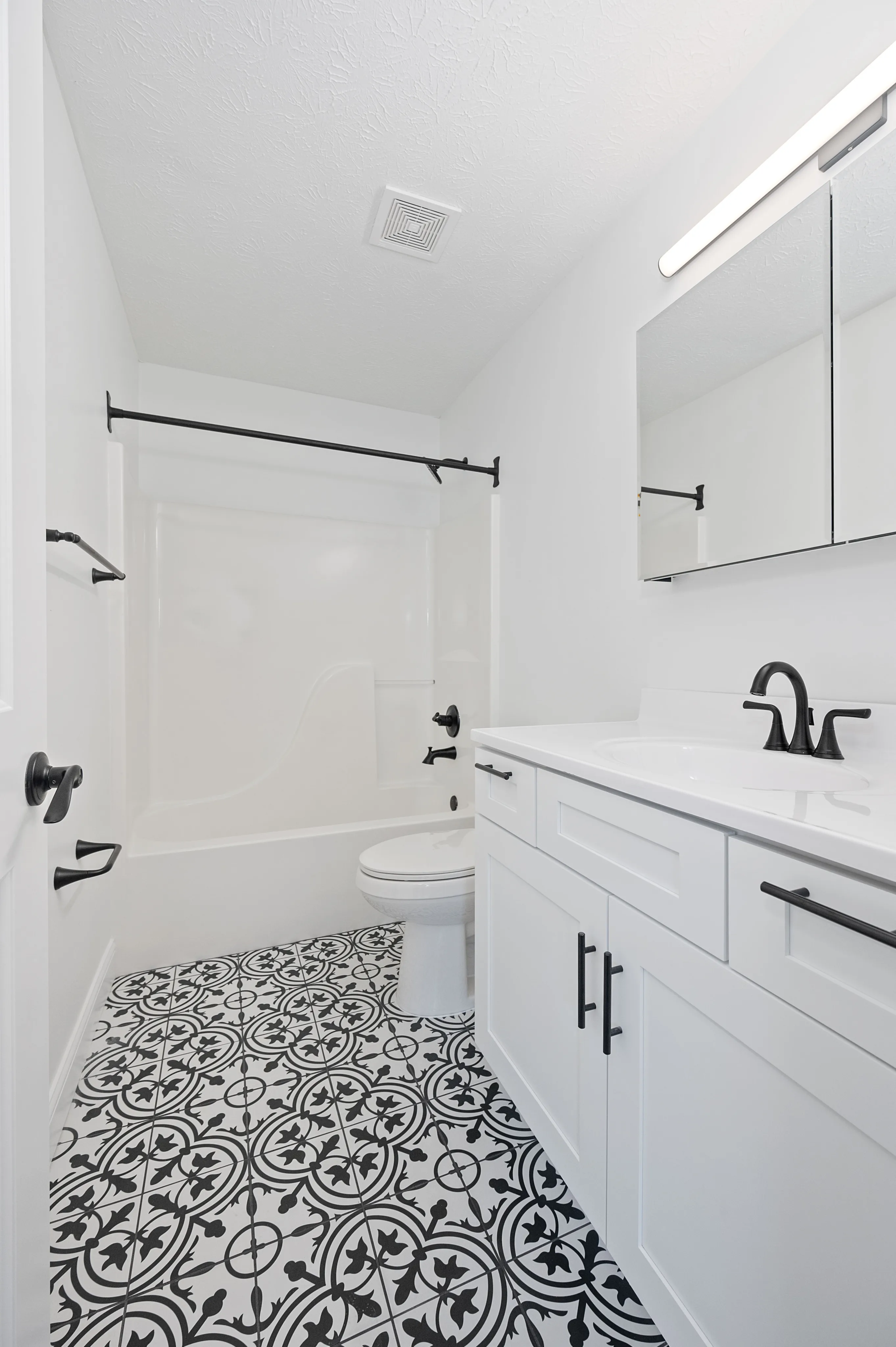 Bright and modern bathroom featuring stylish patterned floor tiles, a sleek vanity, and elegant black fixtures.