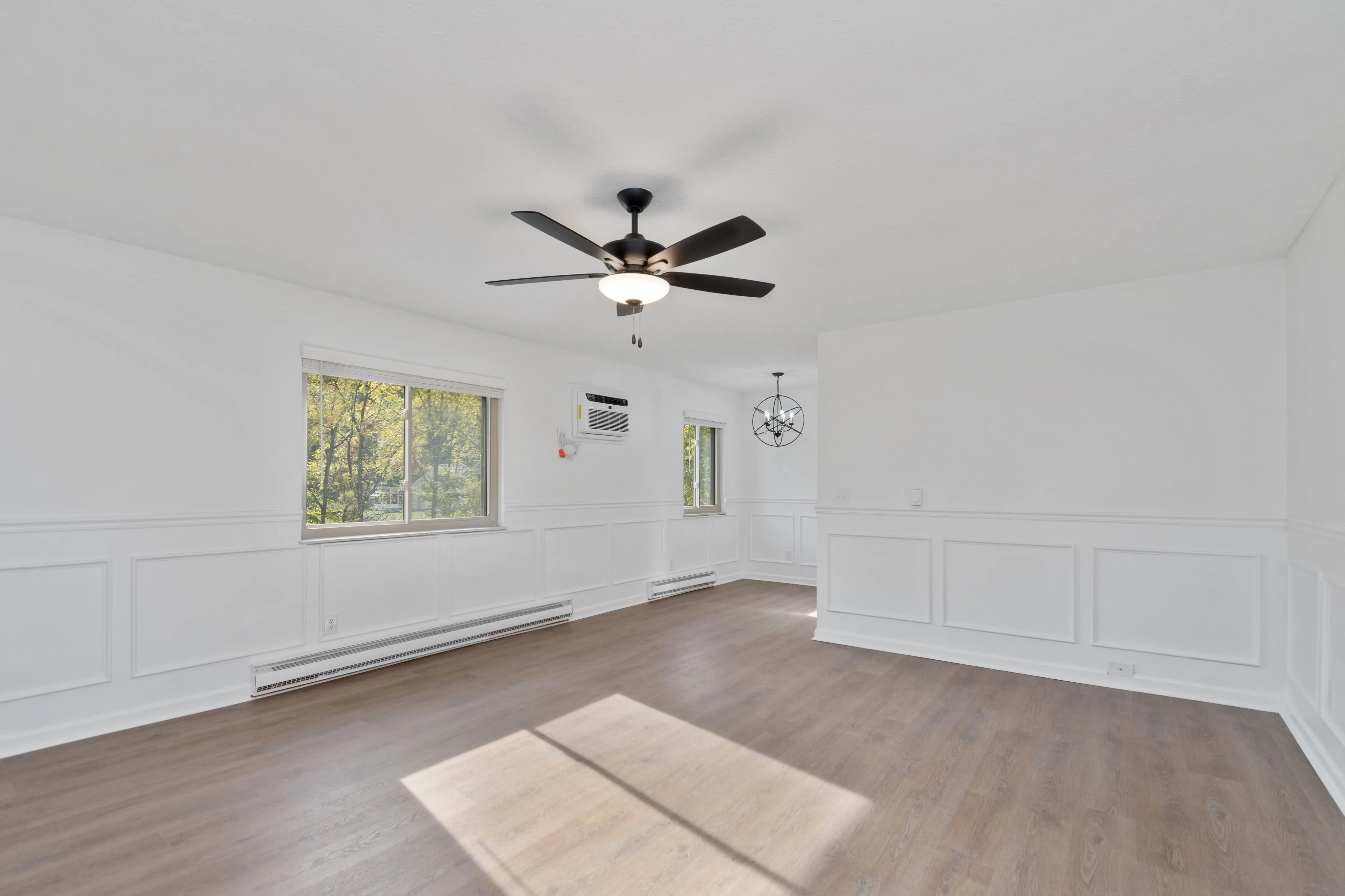 Spacious living room with hardwood floors, large windows, and a modern ceiling fan.