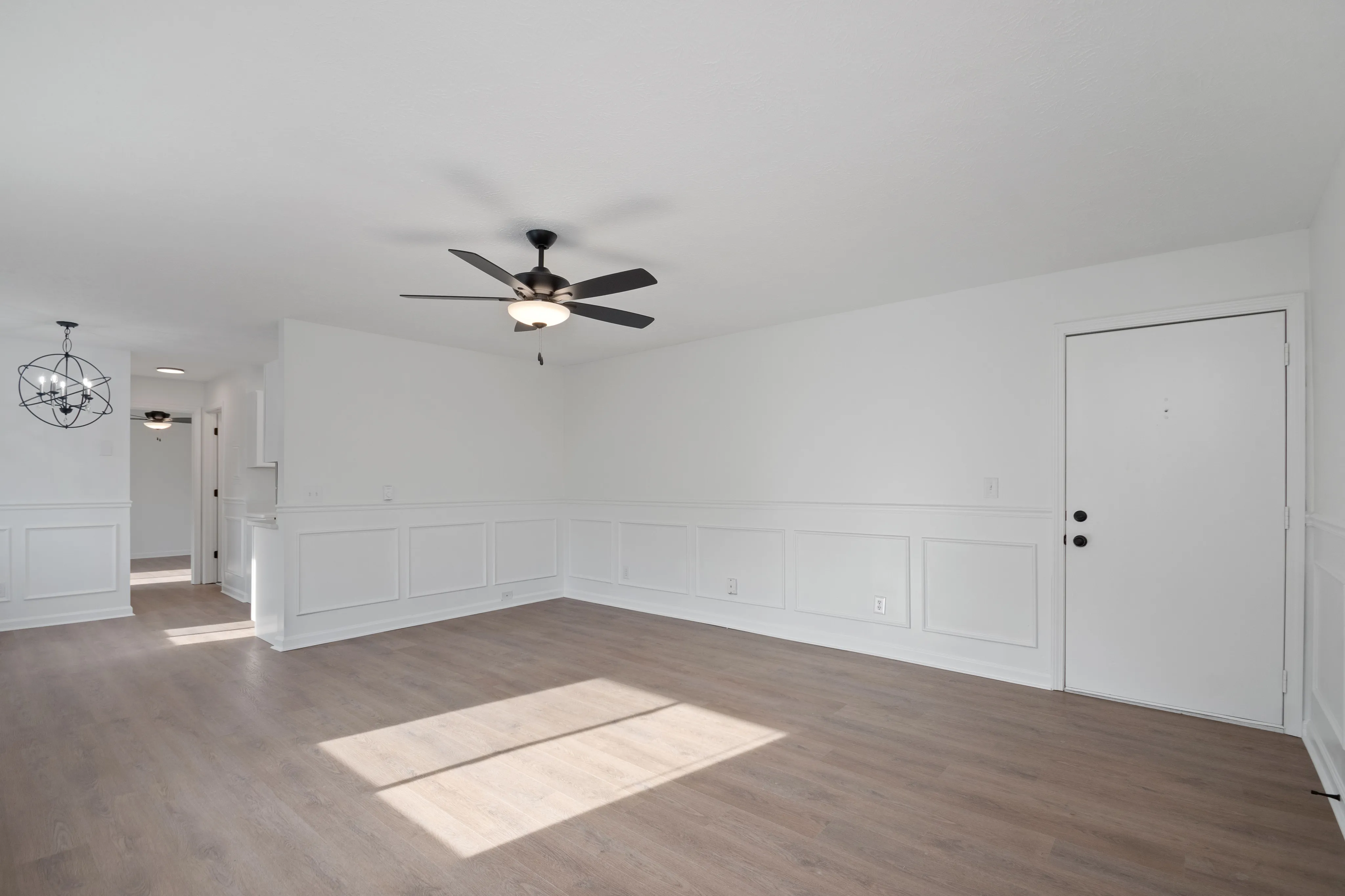 Spacious empty room with elegant wainscoting, ceiling fans, and hardwood flooring.