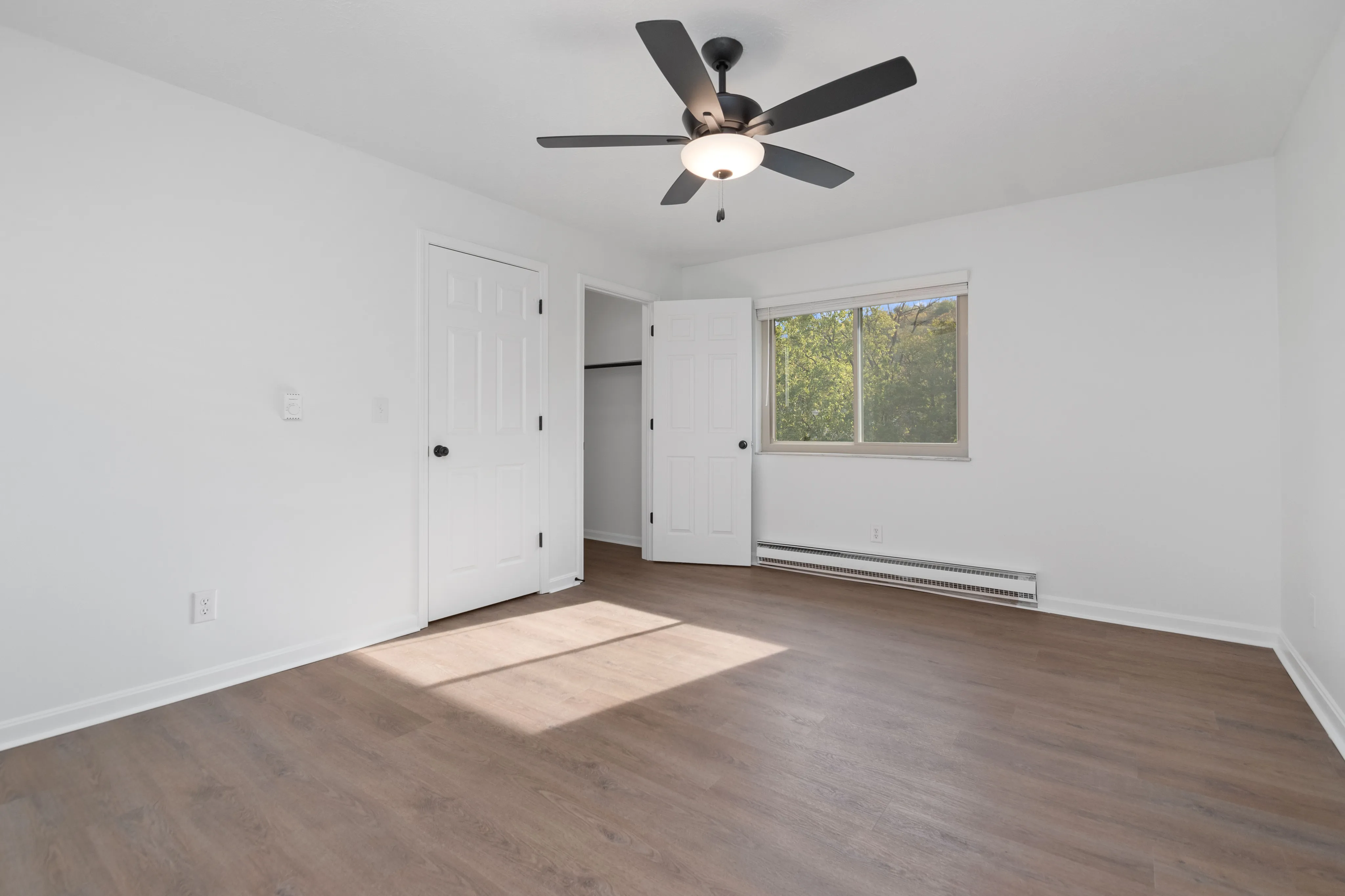 Spacious bedroom with modern ceiling fan, hardwood floors, and large window for natural light.