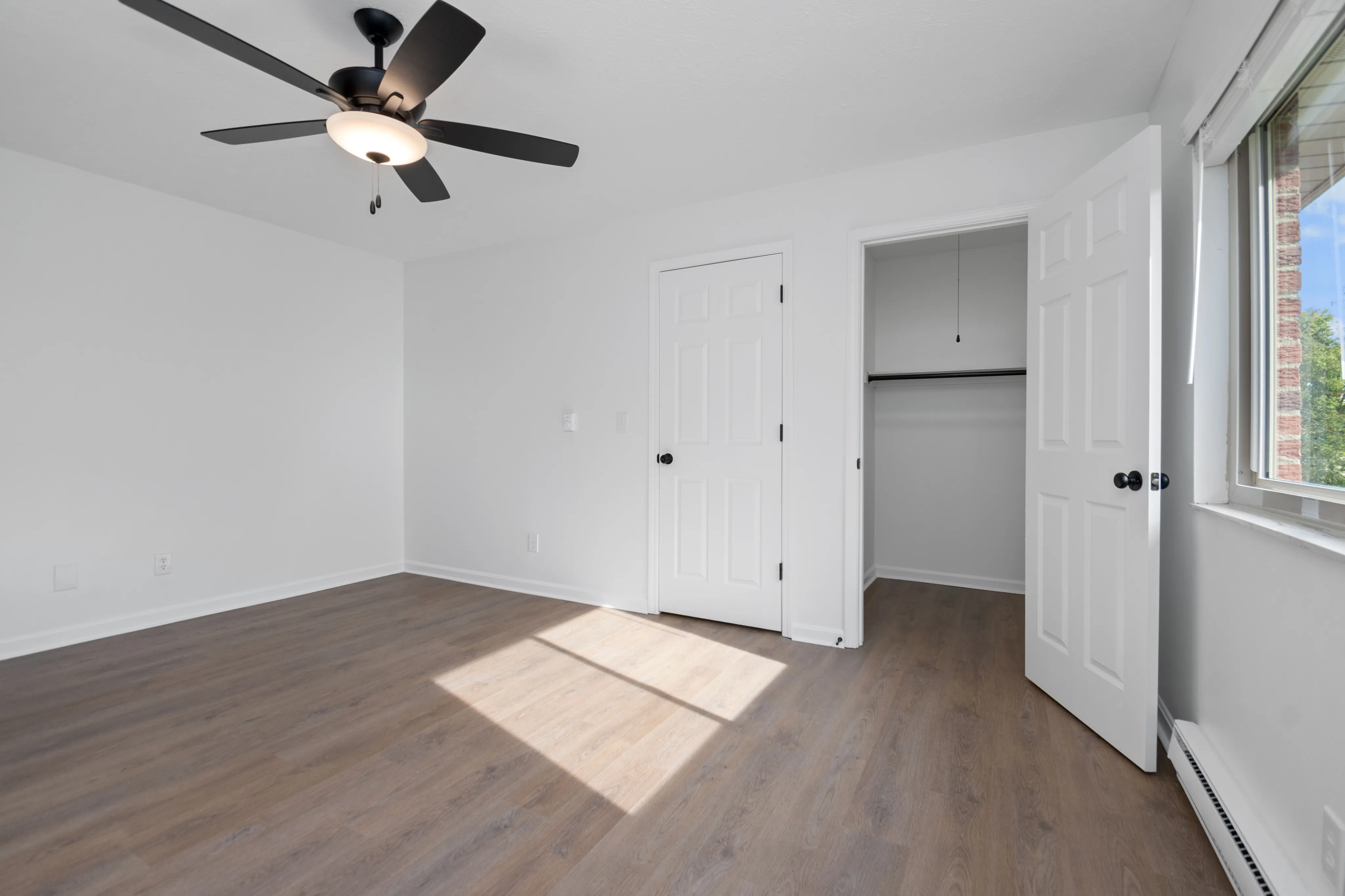 Spacious bedroom with wood flooring, ceiling fan, and open closet space.