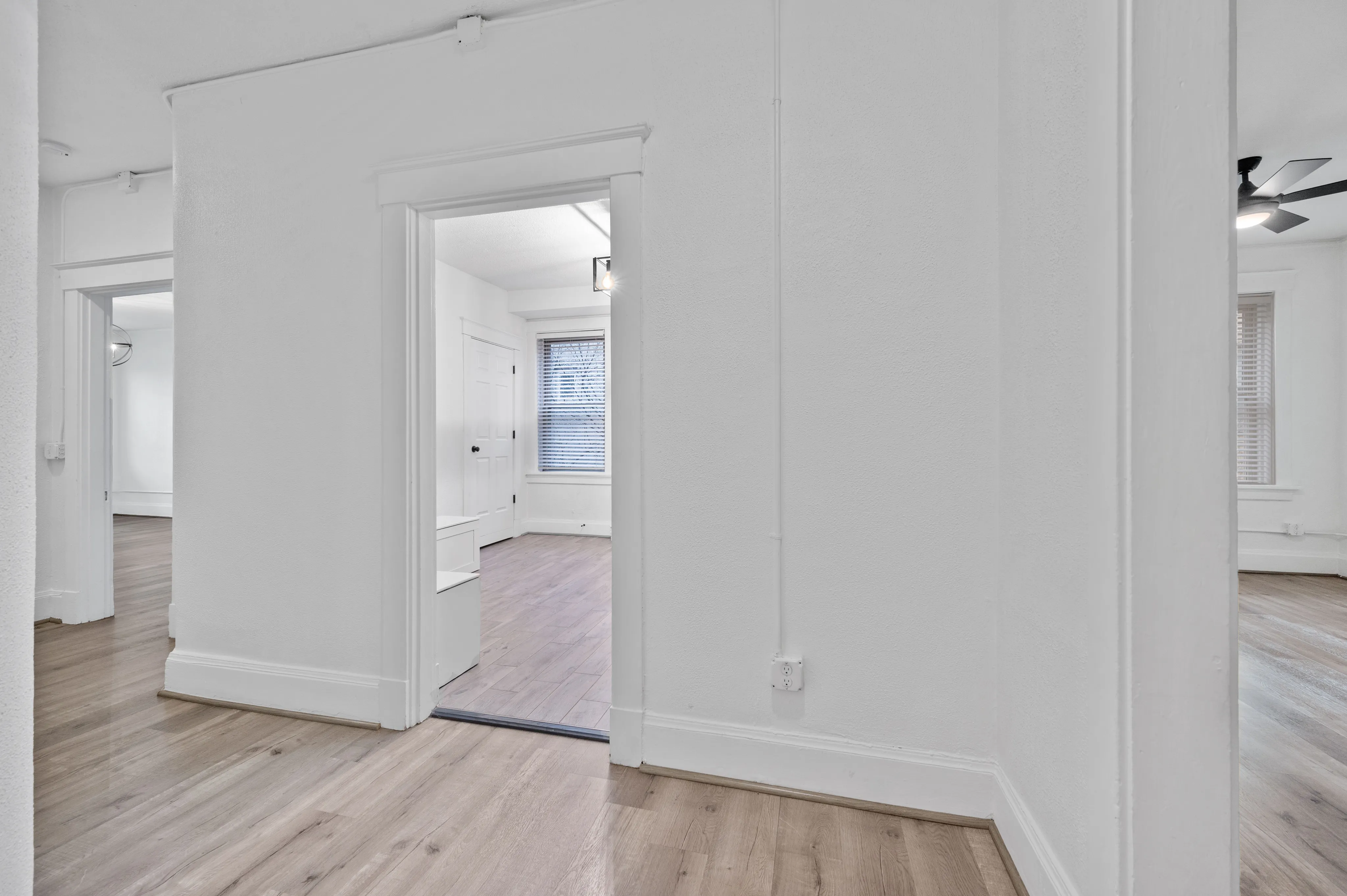 Charming hallway featuring modern light-colored wood flooring and fresh white walls, leading to bright and inviting rooms.