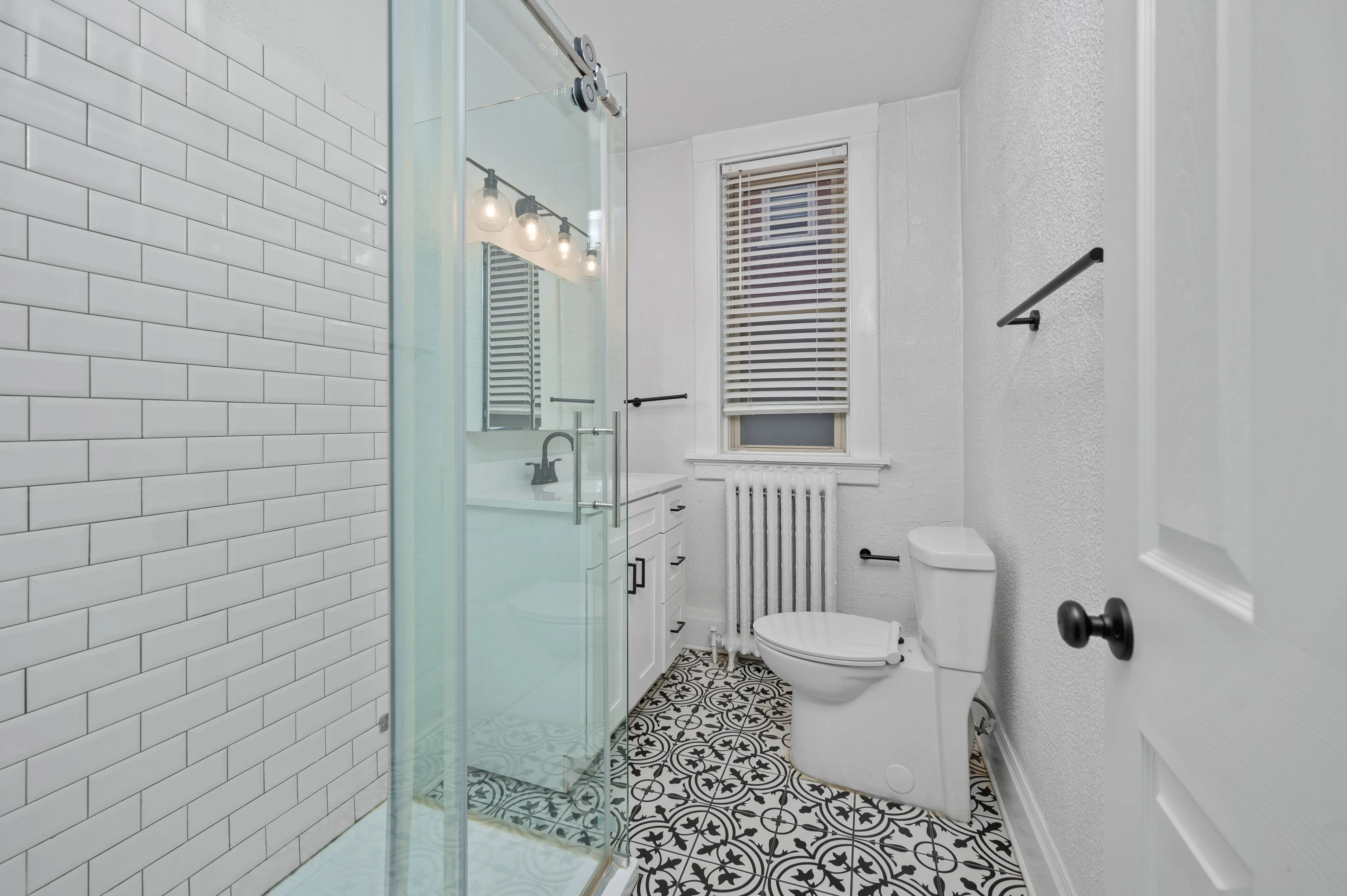 Chic bathroom featuring intricate tile flooring, a sleek glass shower, and contemporary lighting.