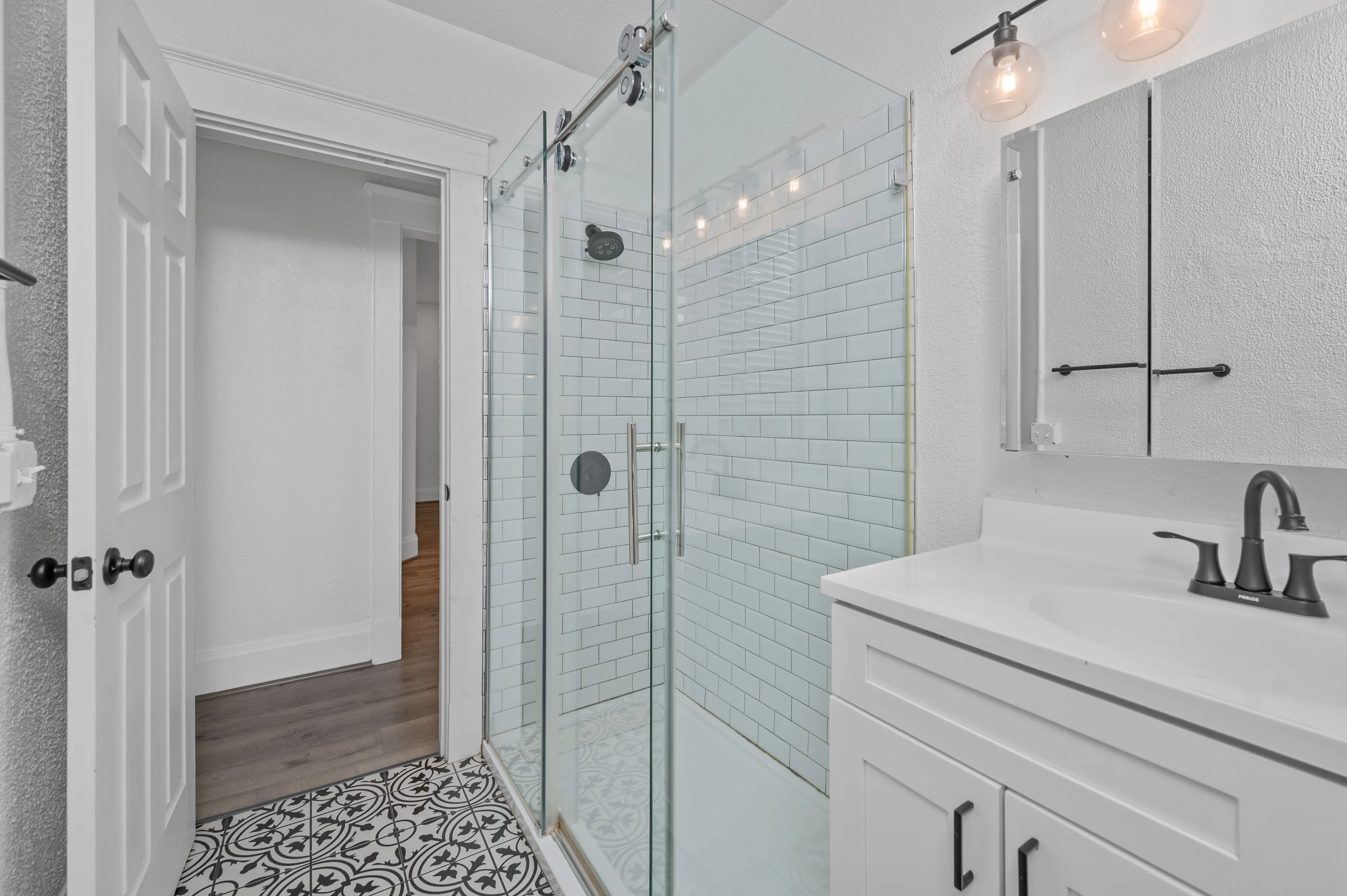 Modern bathroom with elegant glass shower, stylish white subway tiles, and chic patterned flooring.