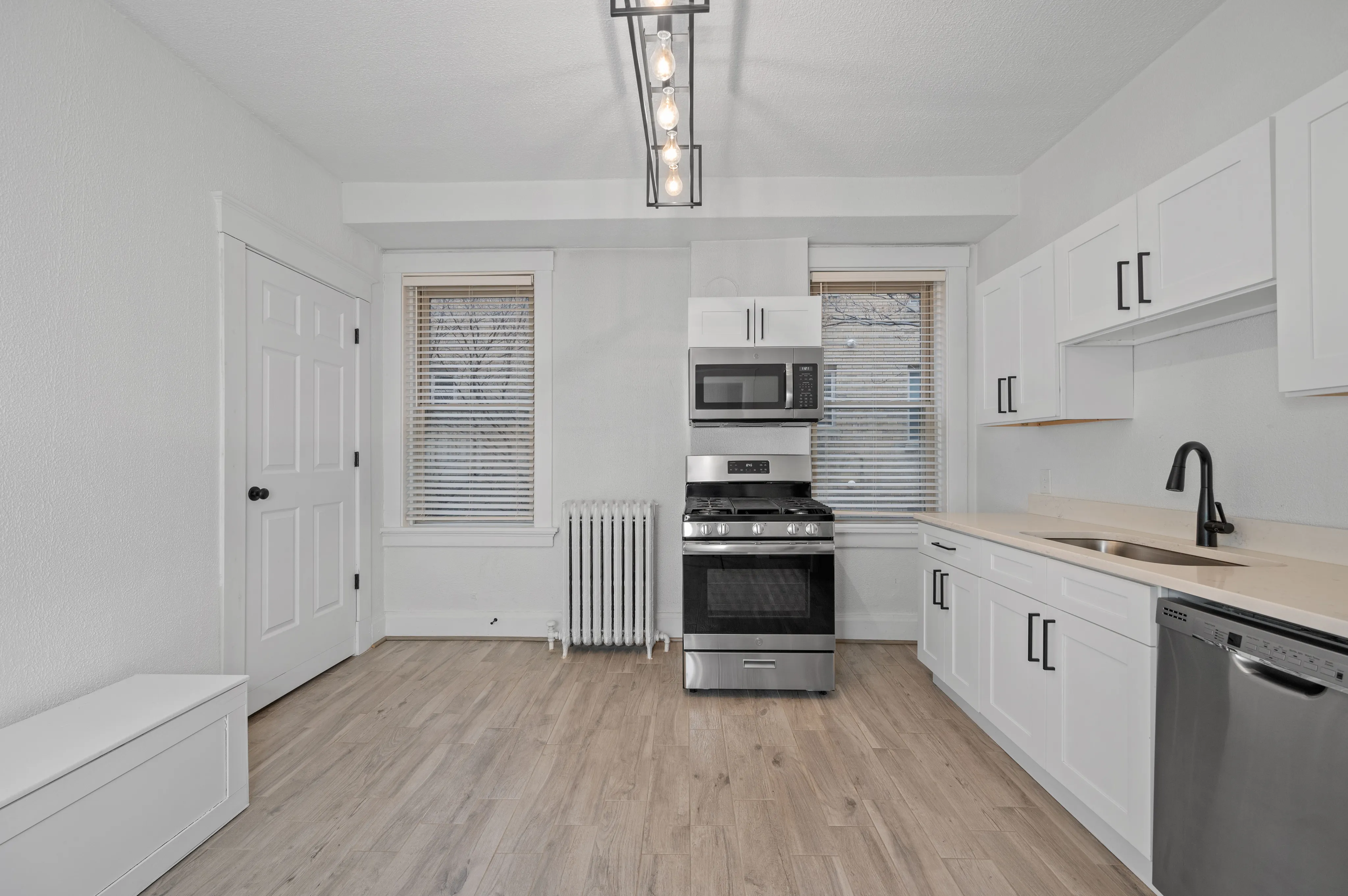 Bright modern kitchen with sleek stainless steel appliances, elegant cabinetry, and stylish light fixture, offering a welcoming and functional cooking space.