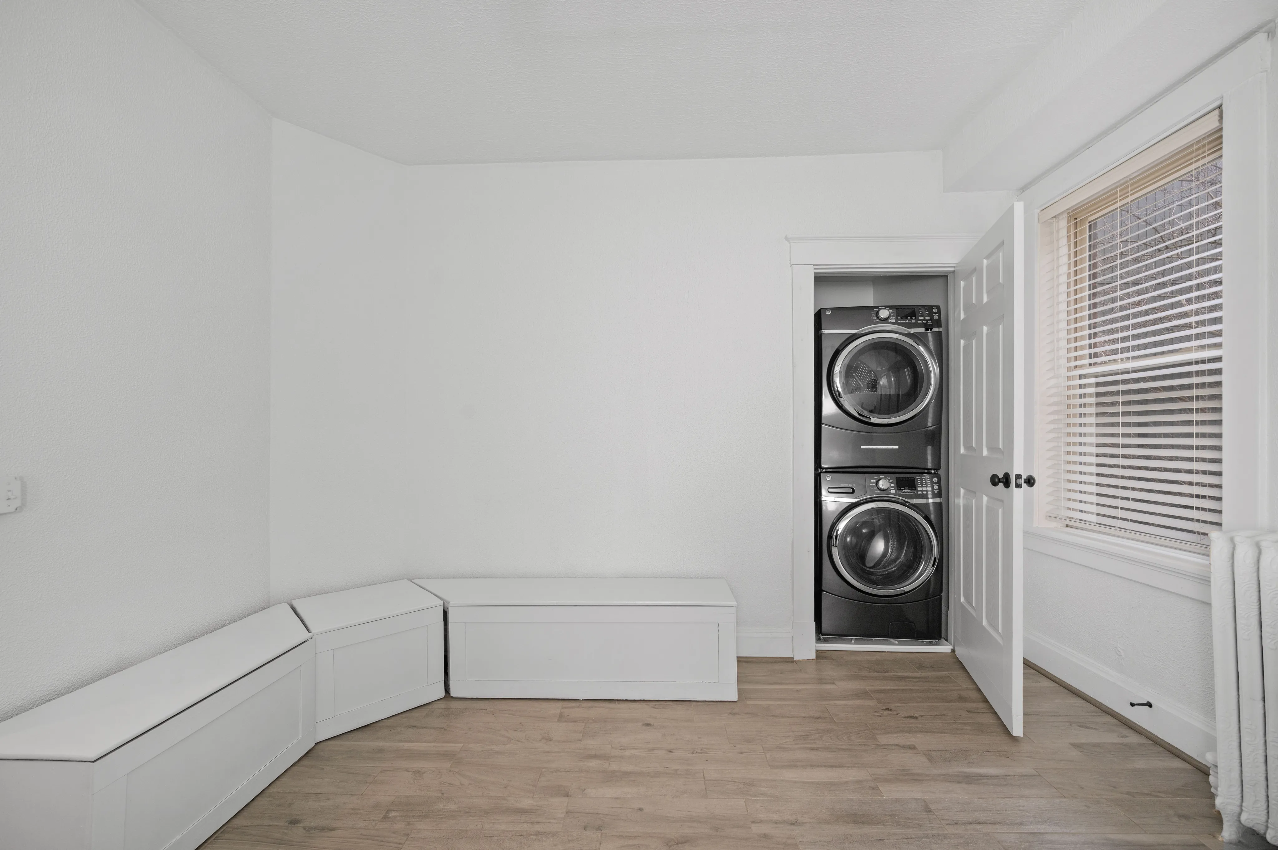 Bright laundry room with stackable washer and dryer, modern seating, and large window for natural light.