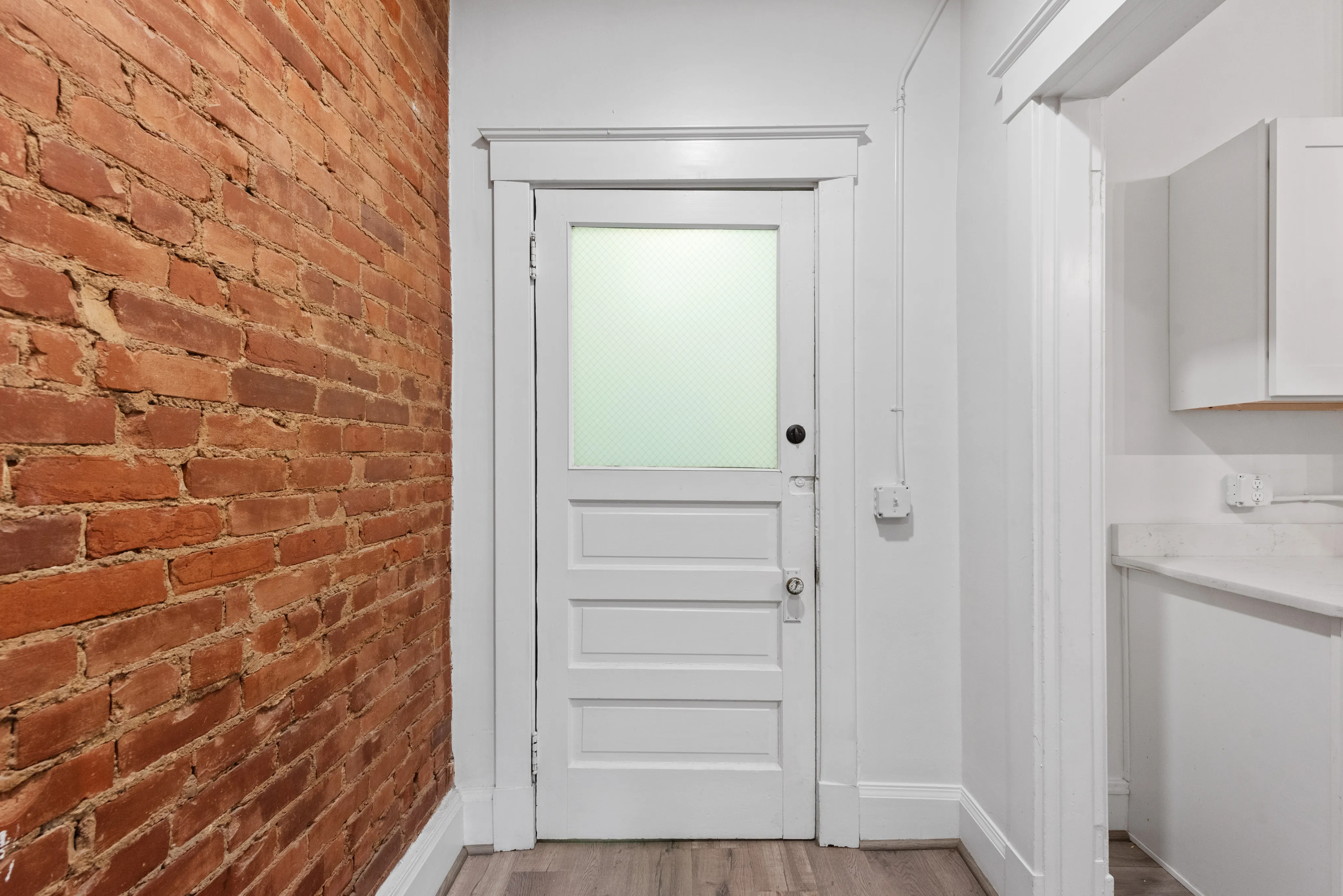 Charming interior entryway with exposed brick wall and classic white door, offering a blend of modern and rustic elegance.