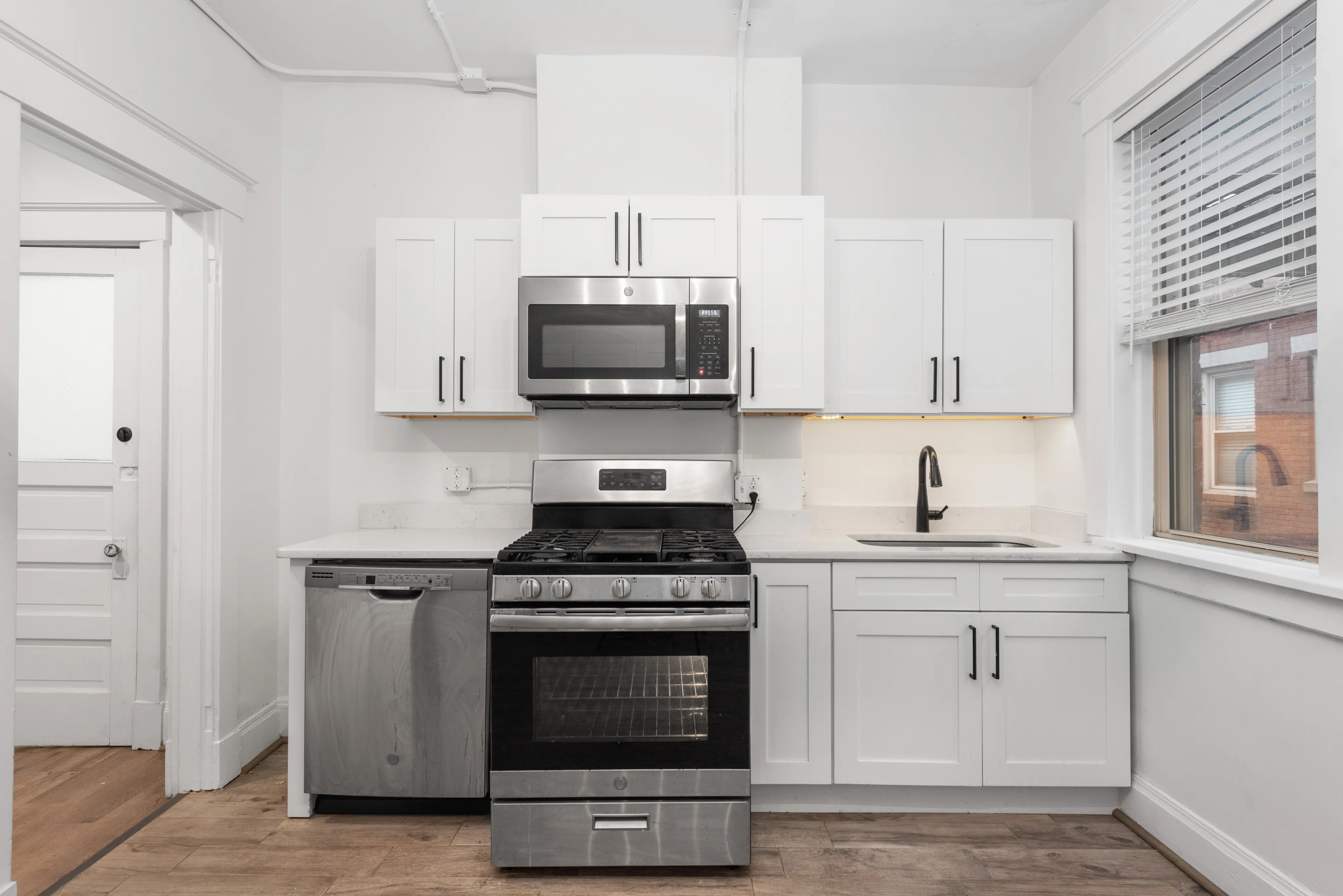 Bright modern kitchen with sleek stainless steel appliances, white cabinetry, and large window offering natural light.