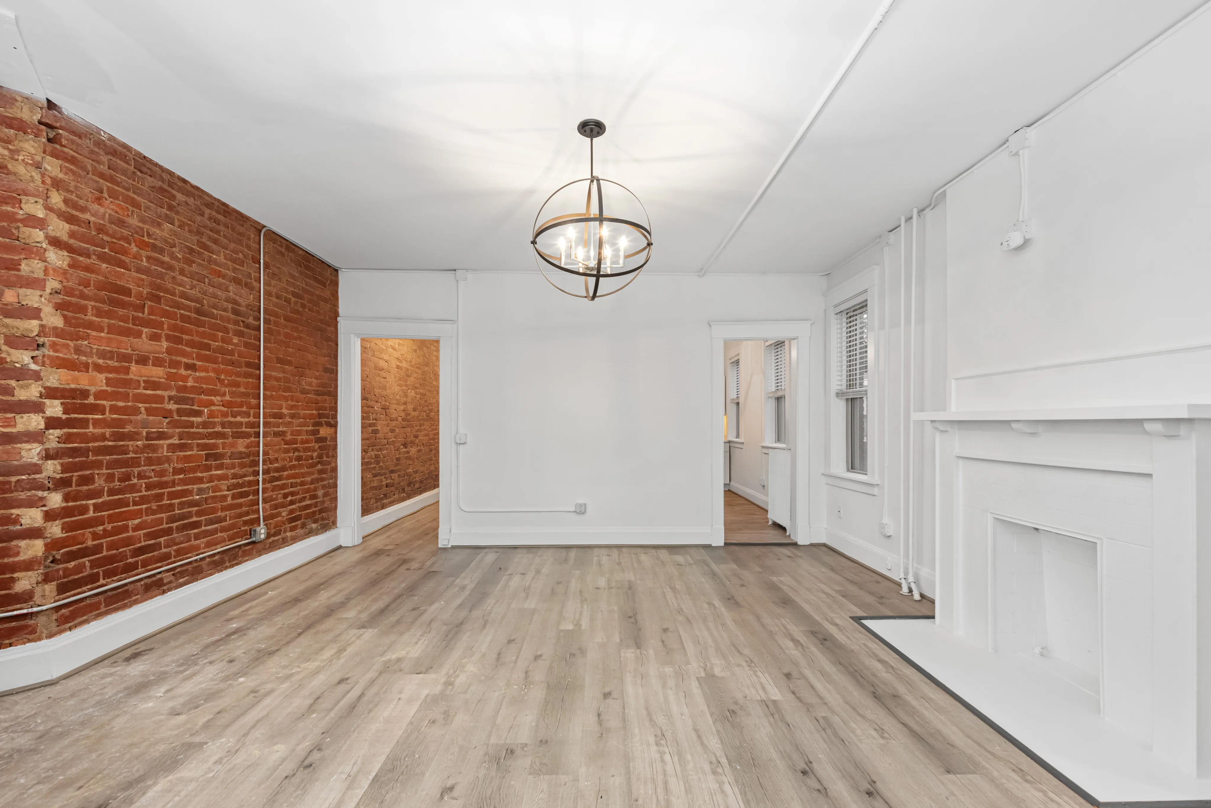 Charming living space with a modern rustic feel, featuring exposed brick walls, elegant light fixture, and sleek wooden floors.