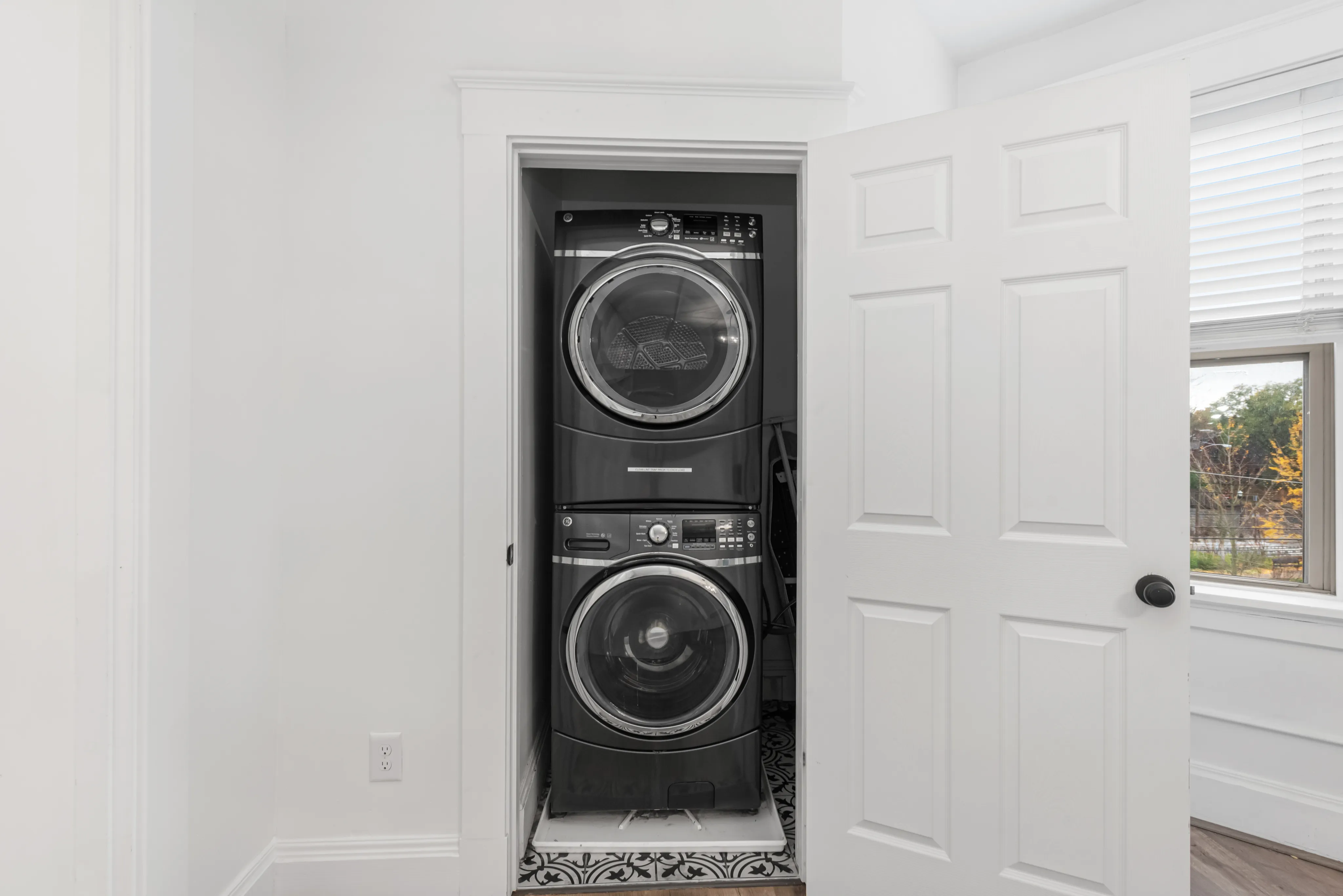 Modern apartment featuring an efficient stacked washer and dryer setup in a bright utility closet, adjacent to a window with natural light.