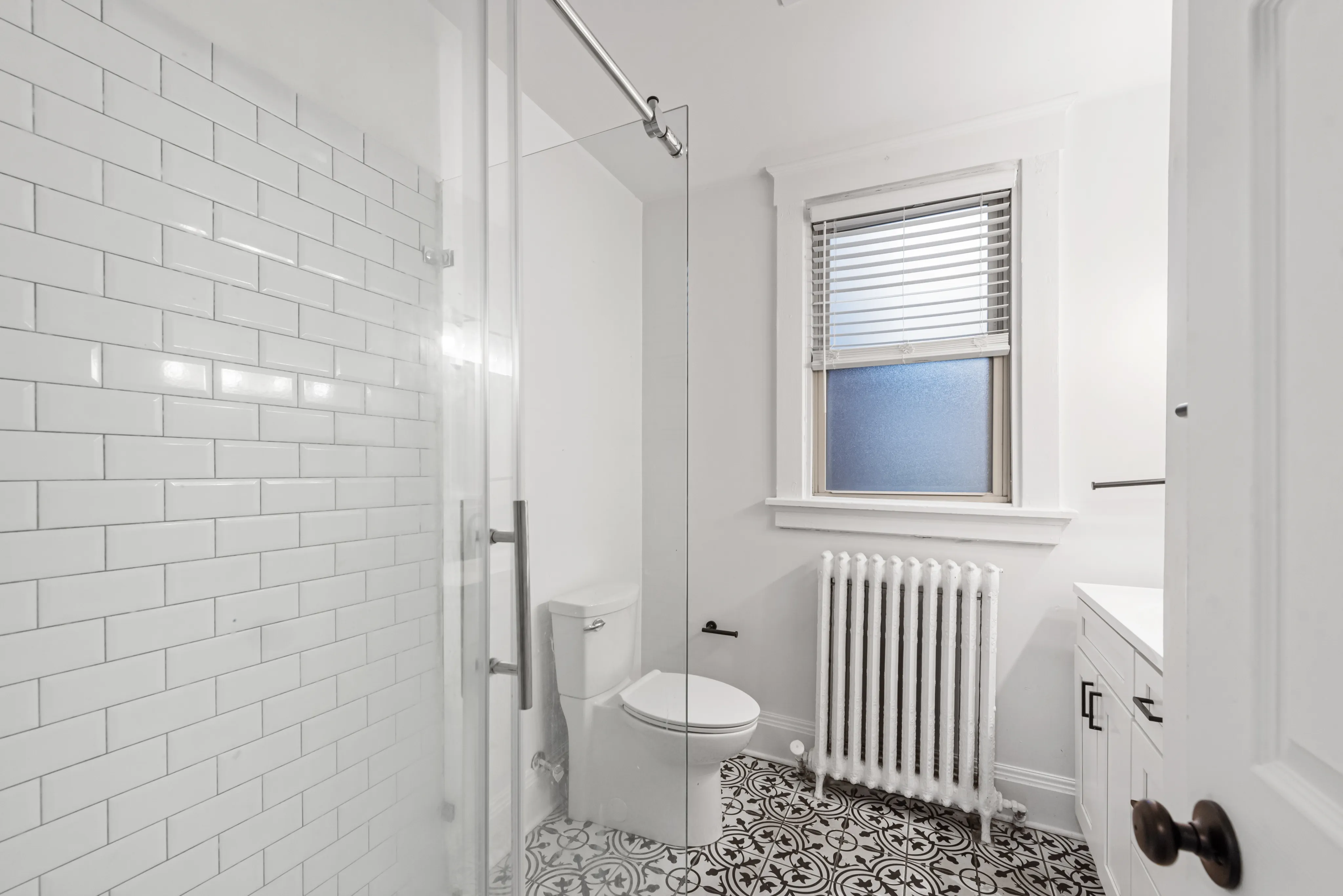 Bright and elegant bathroom featuring modern glass shower, classic white subway tiles, and decorative patterned floor tiles.