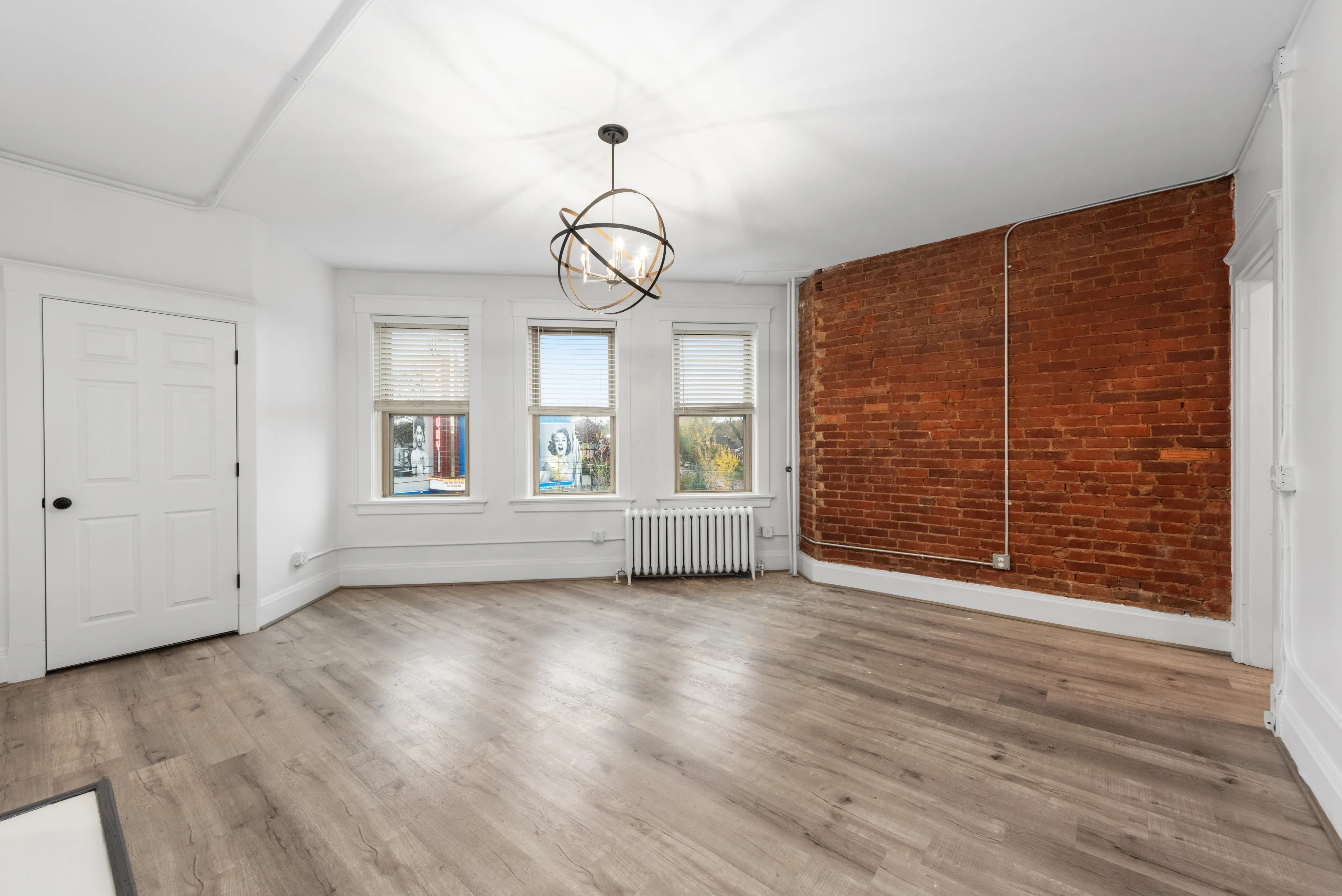 Bright and airy living space with modern lighting, exposed brick wall, and elegant hardwood flooring.