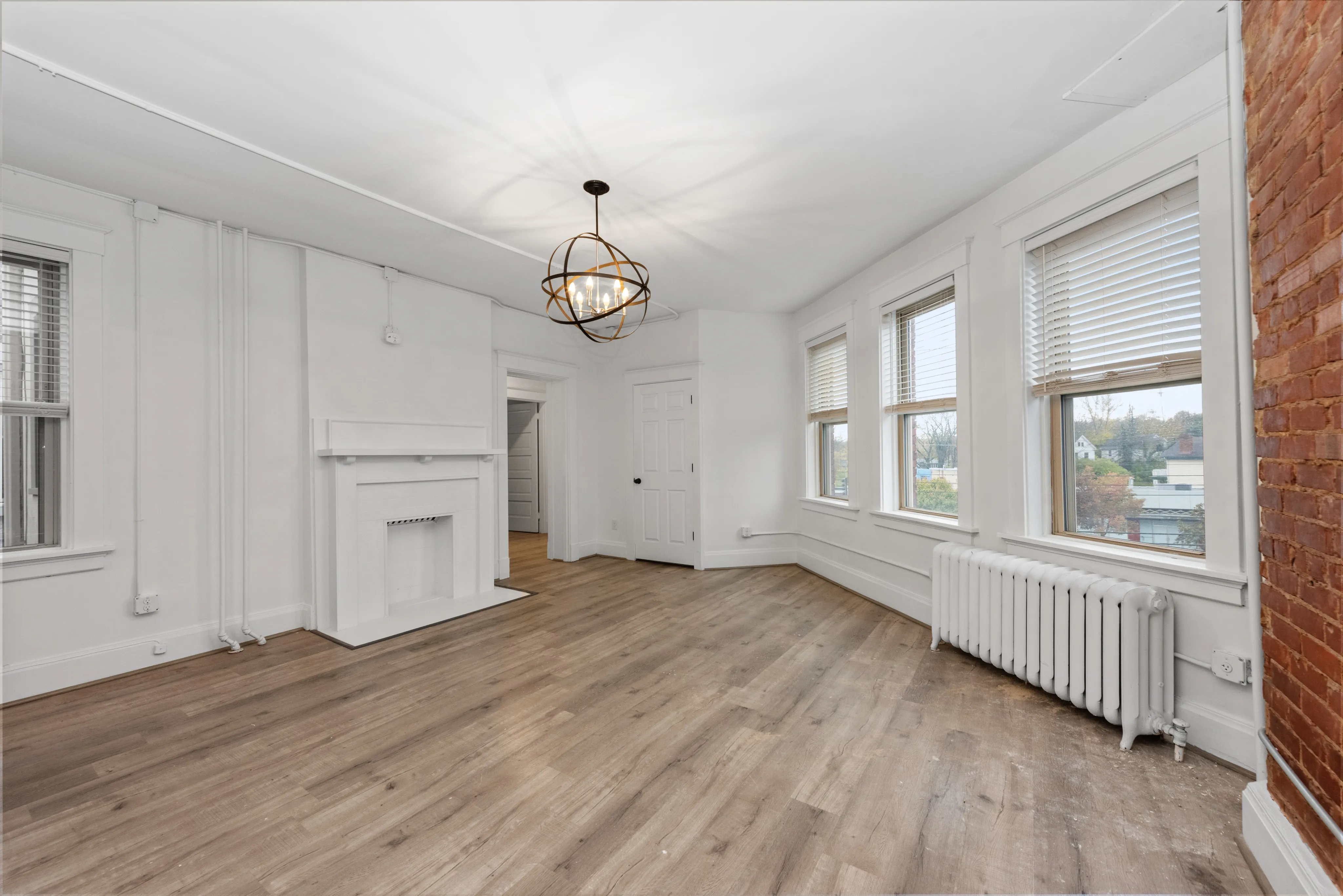 Charming living room with elegant hardwood floors, a classic white fireplace, and large windows offering abundant natural light.