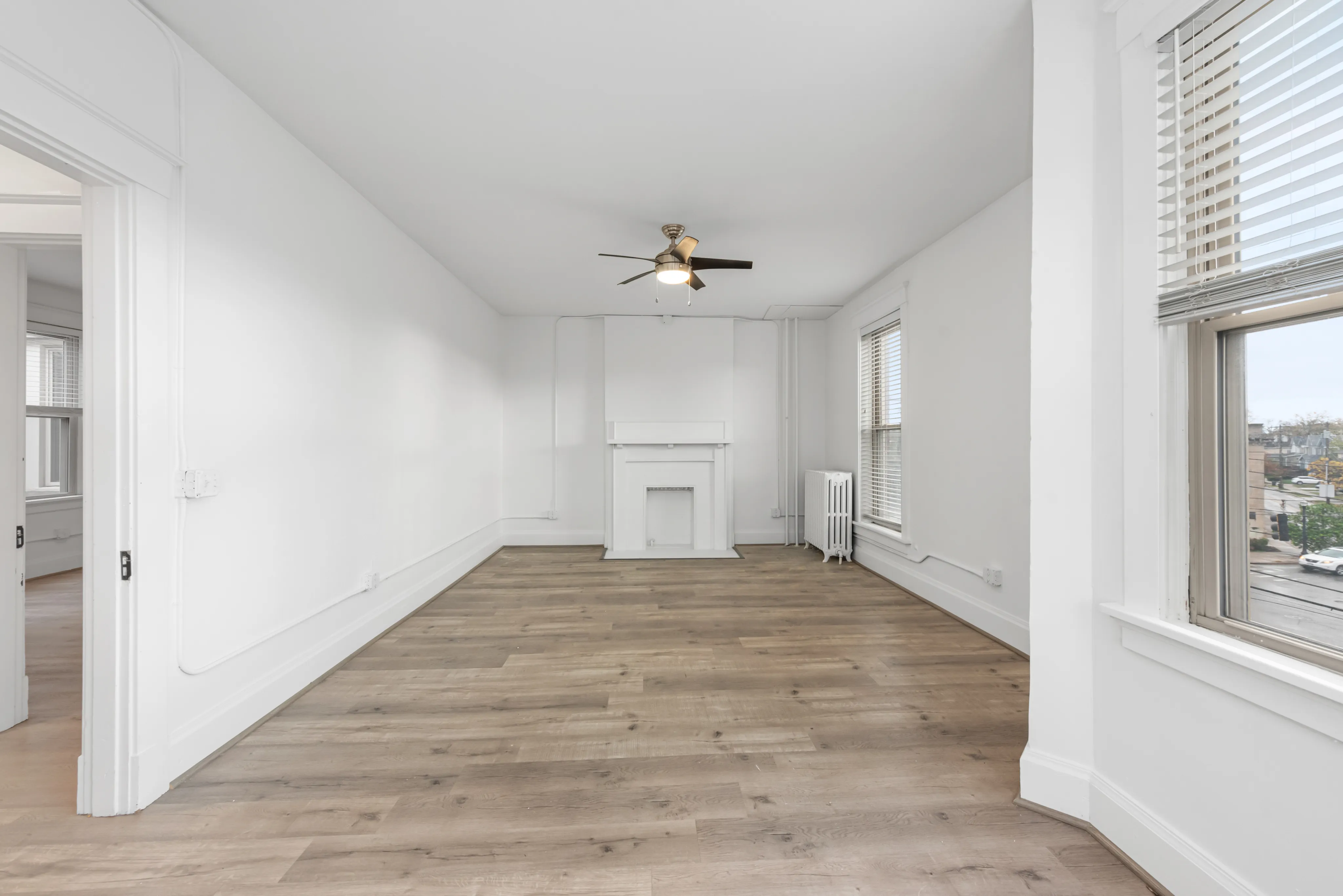Bright, spacious living room with elegant wood flooring, a modern ceiling fan, and large windows for ample natural light.