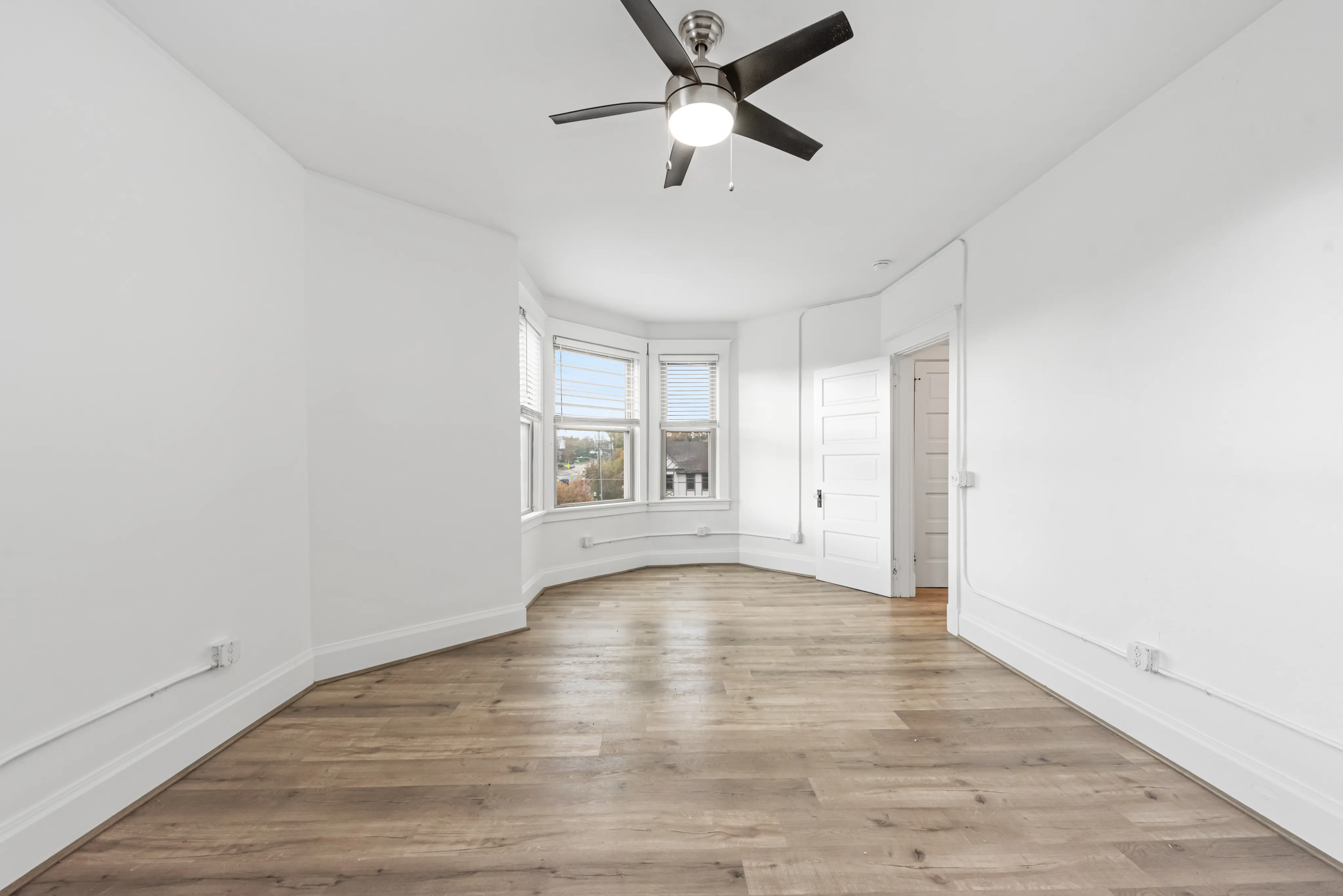 Bright, airy room with elegant hardwood flooring, a ceiling fan, and large bay windows offering scenic views.