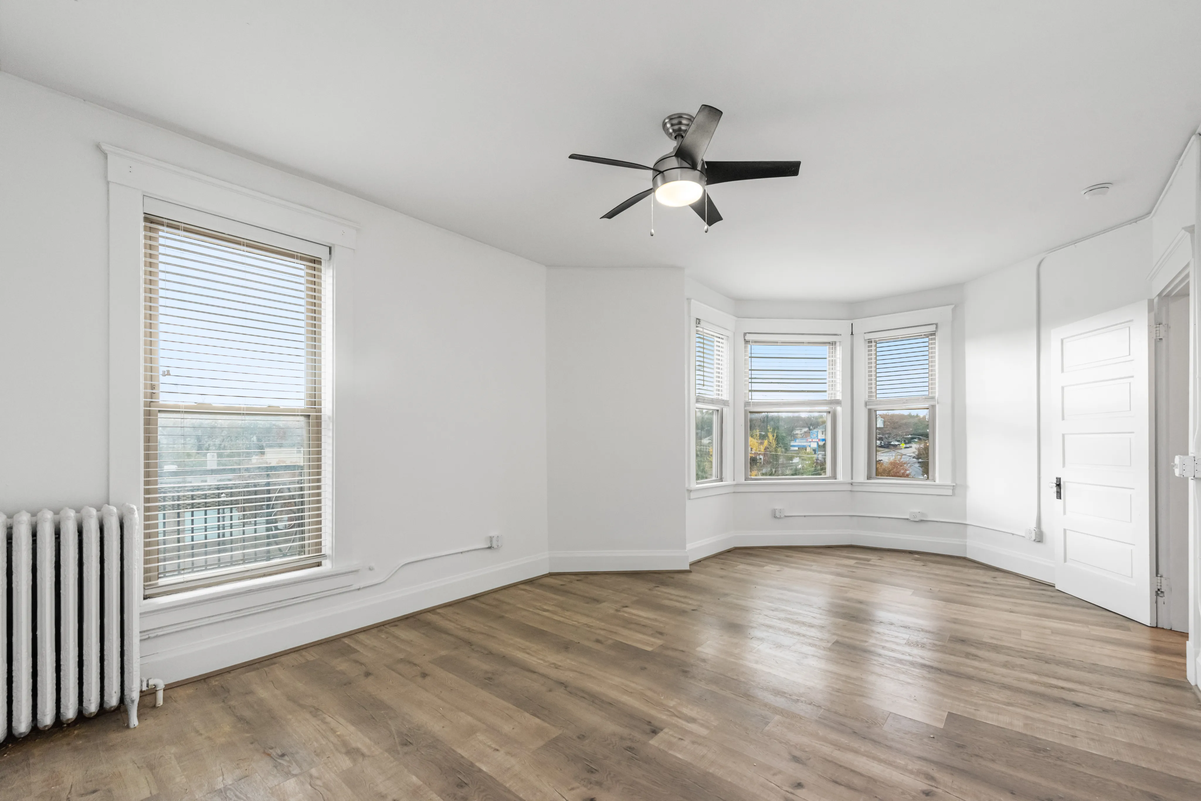 Bright, spacious room with elegant hardwood floors, large windows, and a modern ceiling fan.