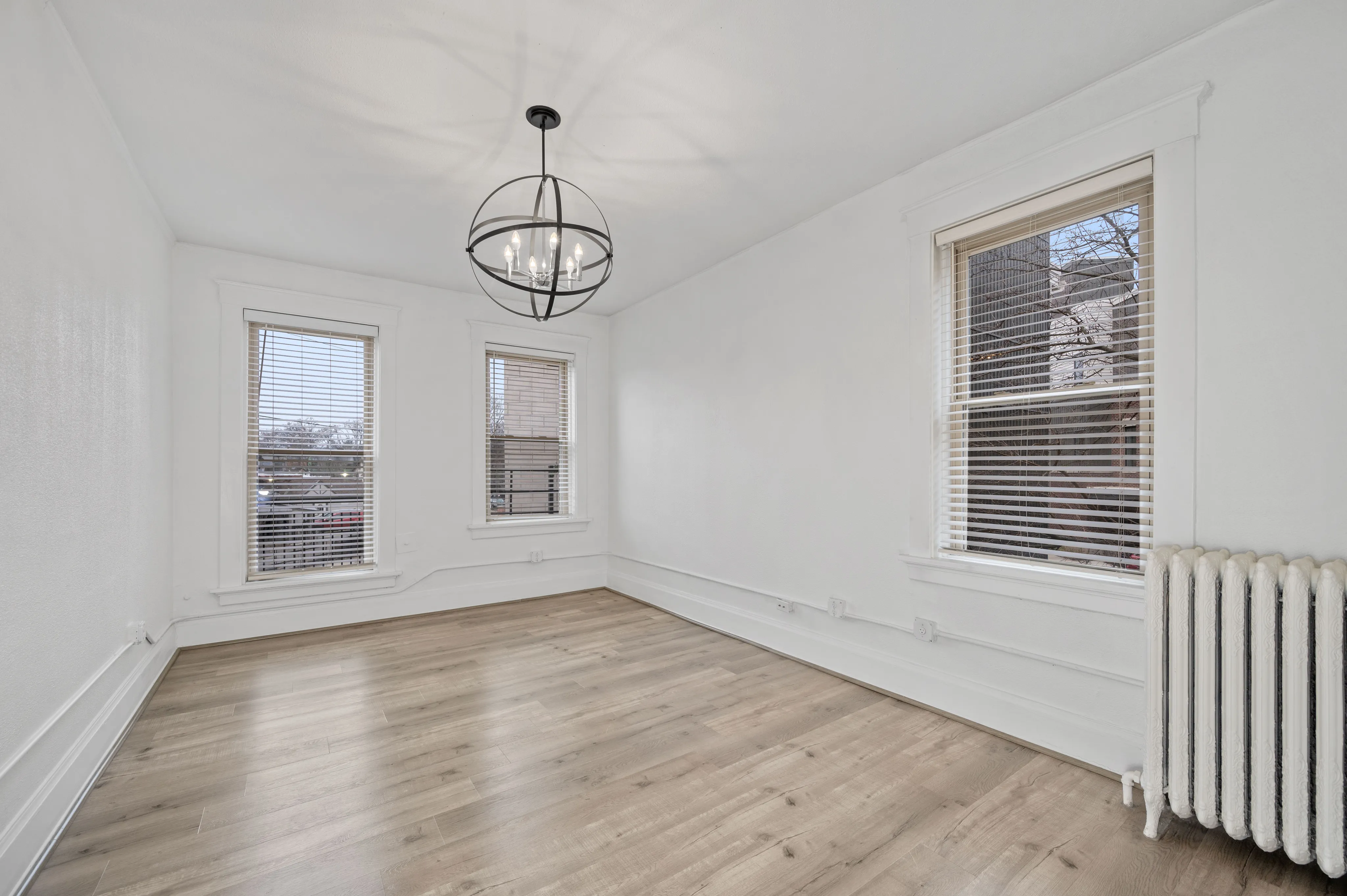 Bright and airy room with elegant light fixture, featuring large windows and sleek hardwood floors.