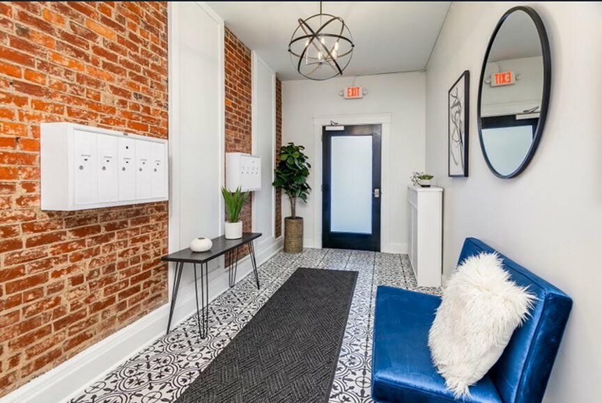 Contemporary apartment foyer with chic exposed brick, elegant patterned tiles, and plush blue seating, offering a welcoming atmosphere.