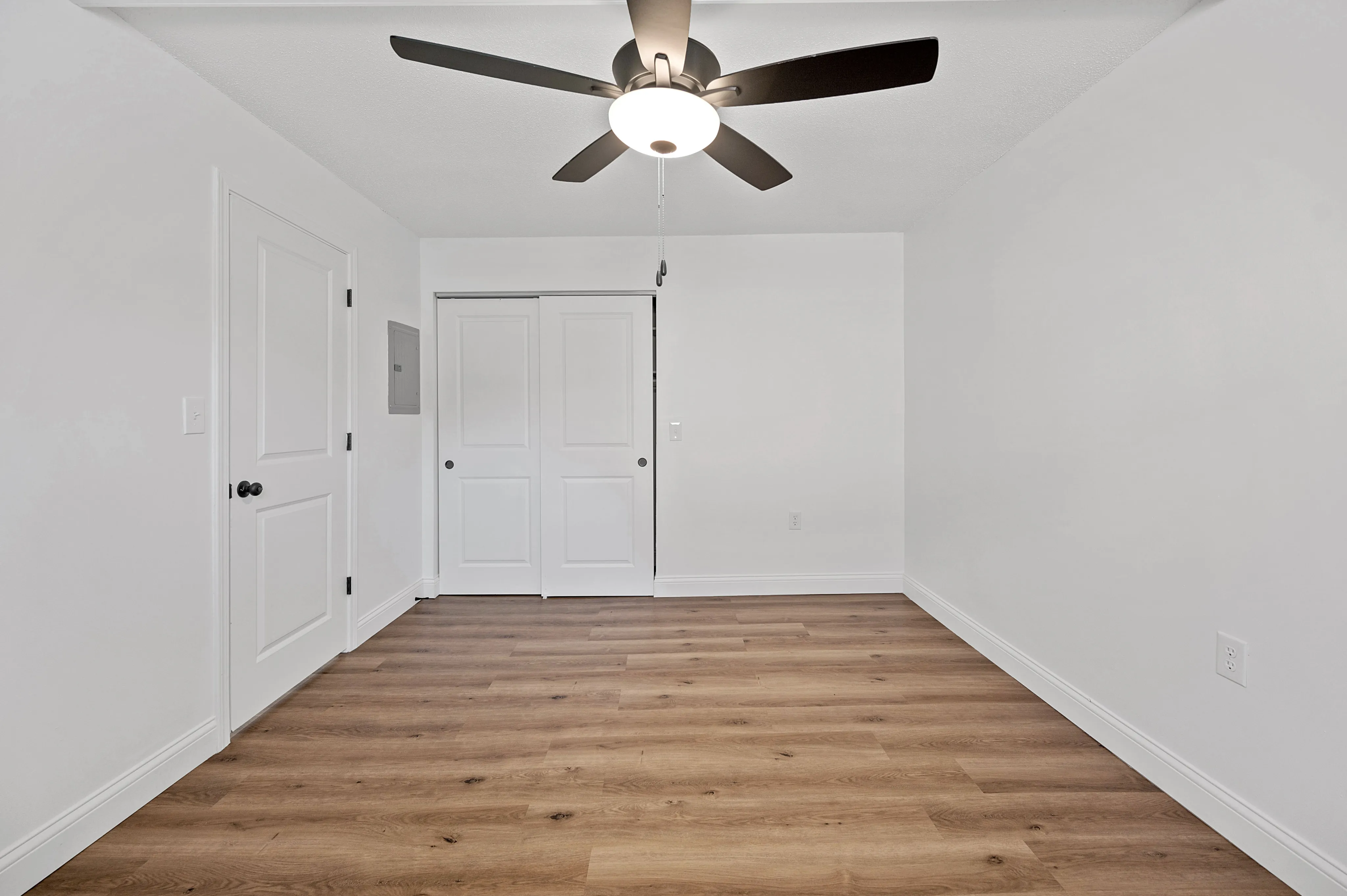 Modern room with sleek ceiling fan, elegant hardwood flooring, and pristine white walls, perfect for a peaceful retreat.