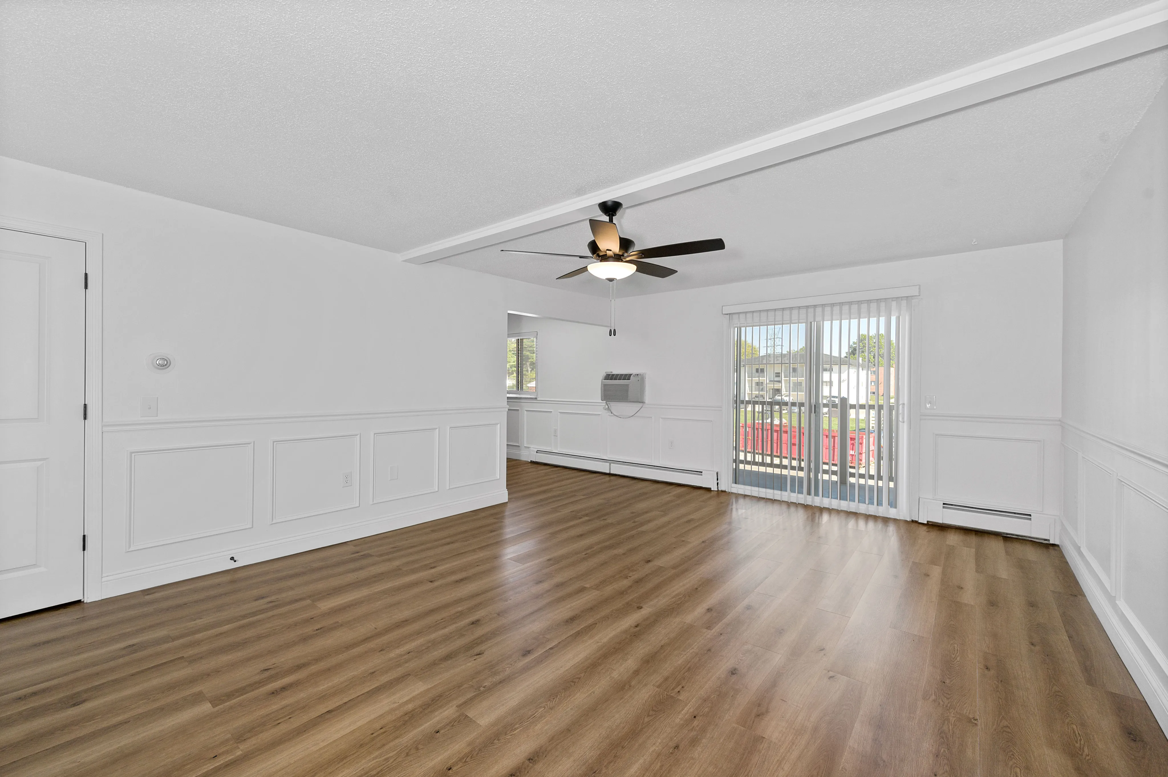 Bright, spacious living room with elegant wood flooring, modern ceiling fan, and large sliding glass doors leading to a balcony.