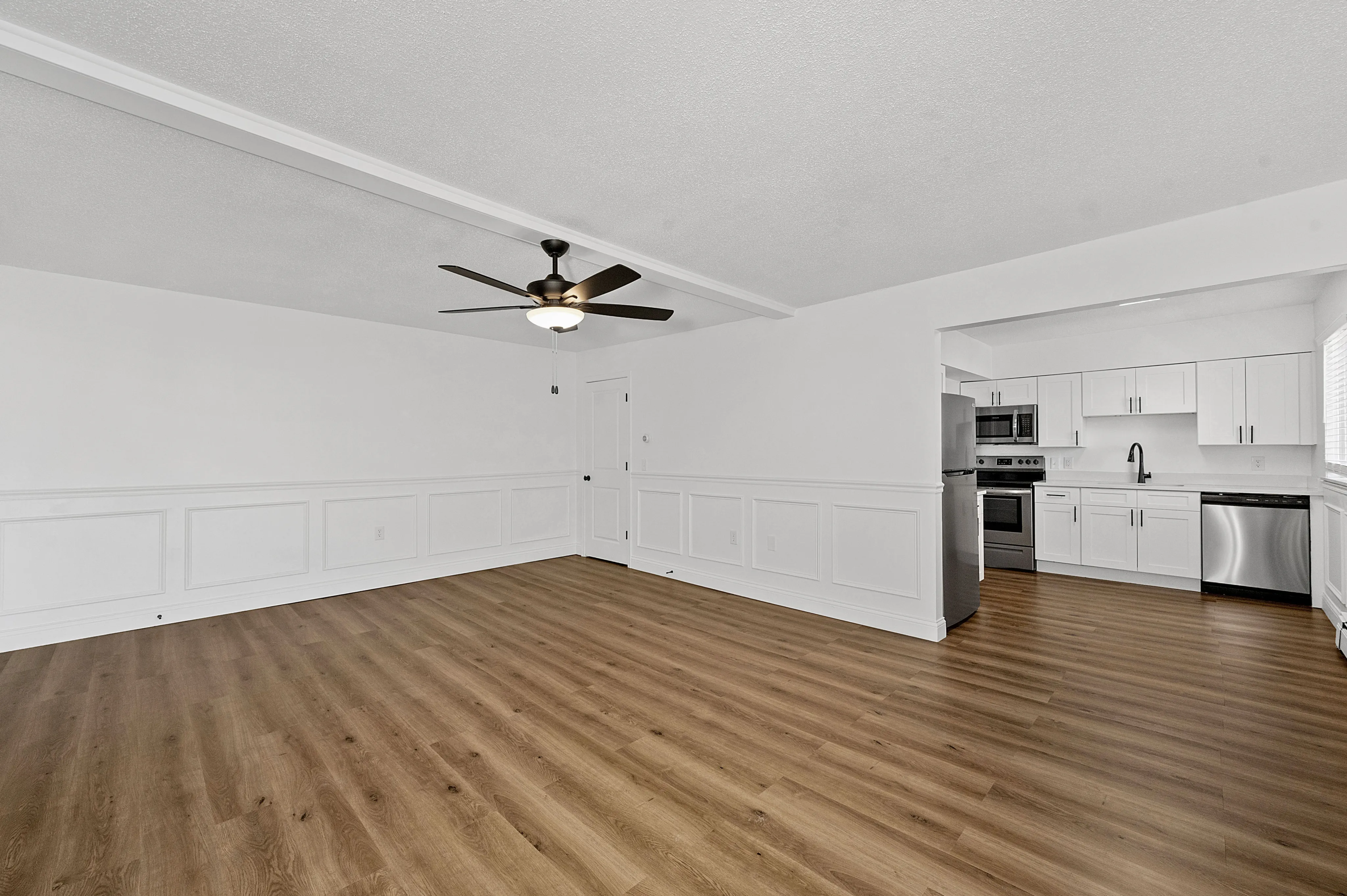 Modern open-concept living area with elegant wooden flooring, ceiling fan, and sleek kitchen featuring stainless steel appliances.