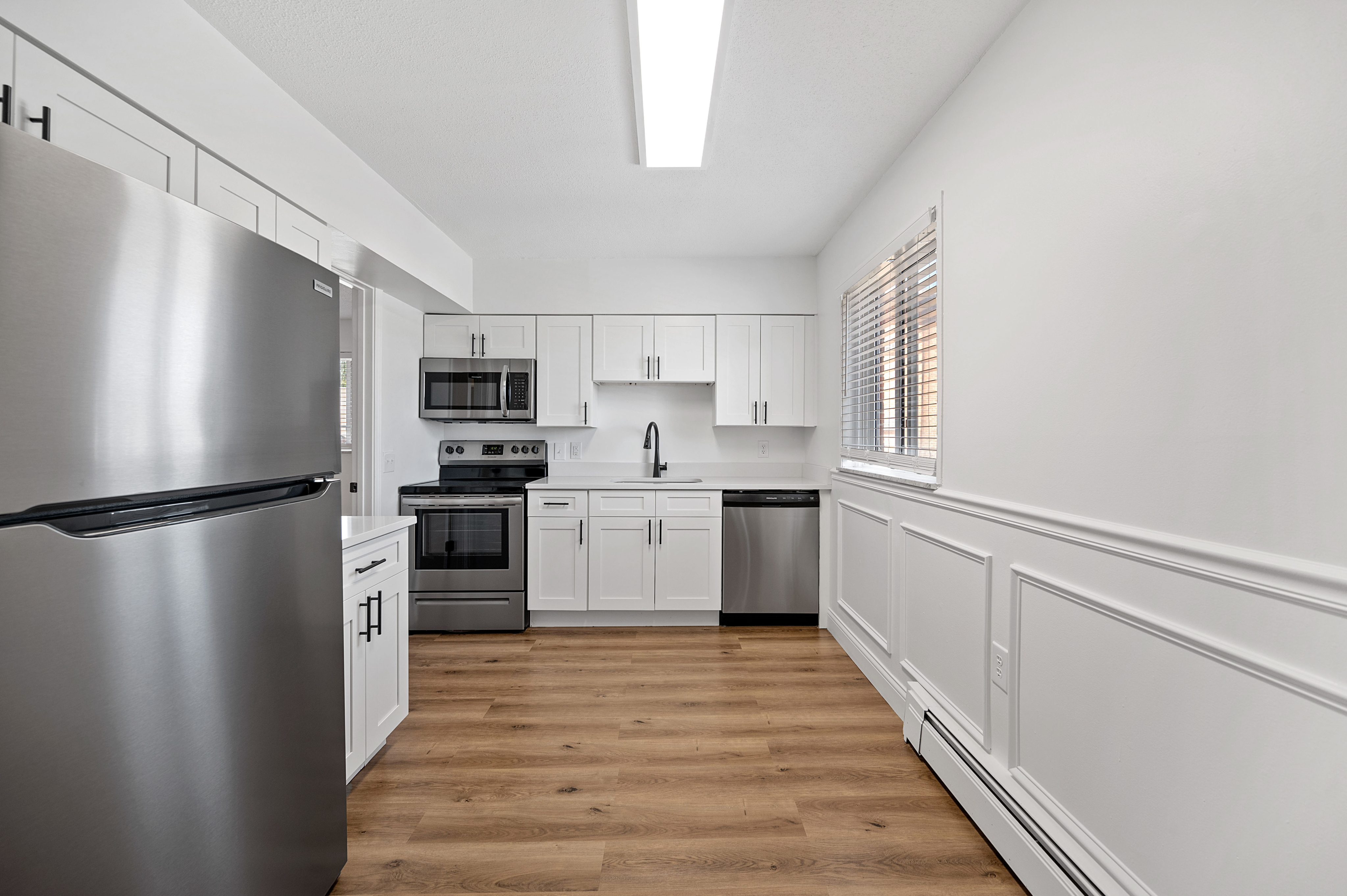 Modern kitchen featuring sleek stainless steel appliances, elegant white cabinetry, and warm wooden flooring.