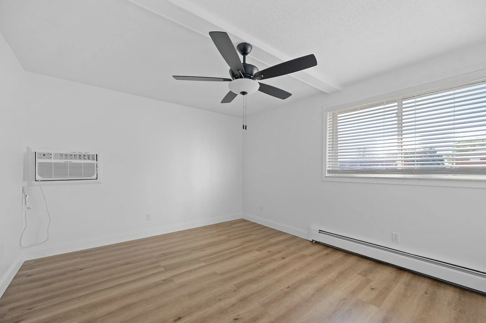 Bright and airy bedroom with modern ceiling fan, sleek blinds, and elegant wooden floors.