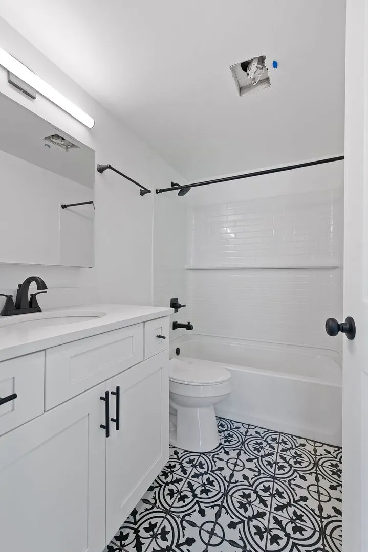 Chic modern bathroom with elegant black and white patterned tiles, a sleek white vanity, and contemporary fixtures.