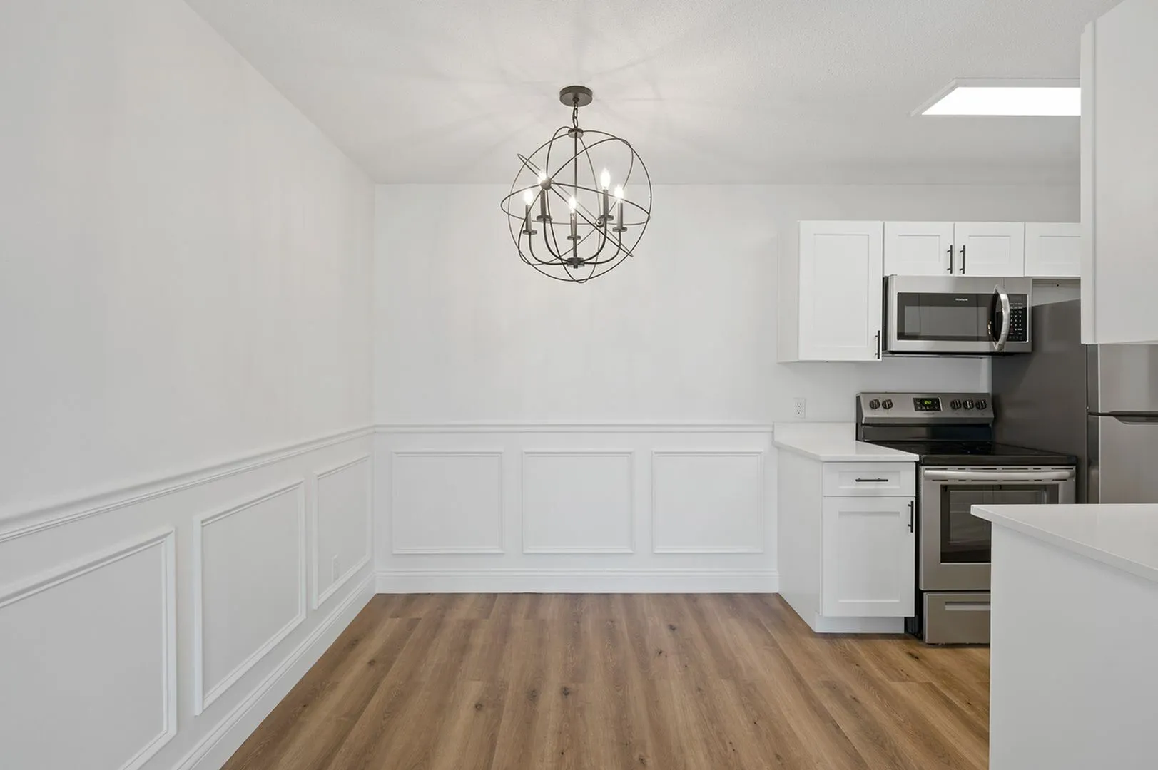 Elegant dining area with modern chandelier and sleek kitchen featuring stainless steel appliances and white cabinetry.