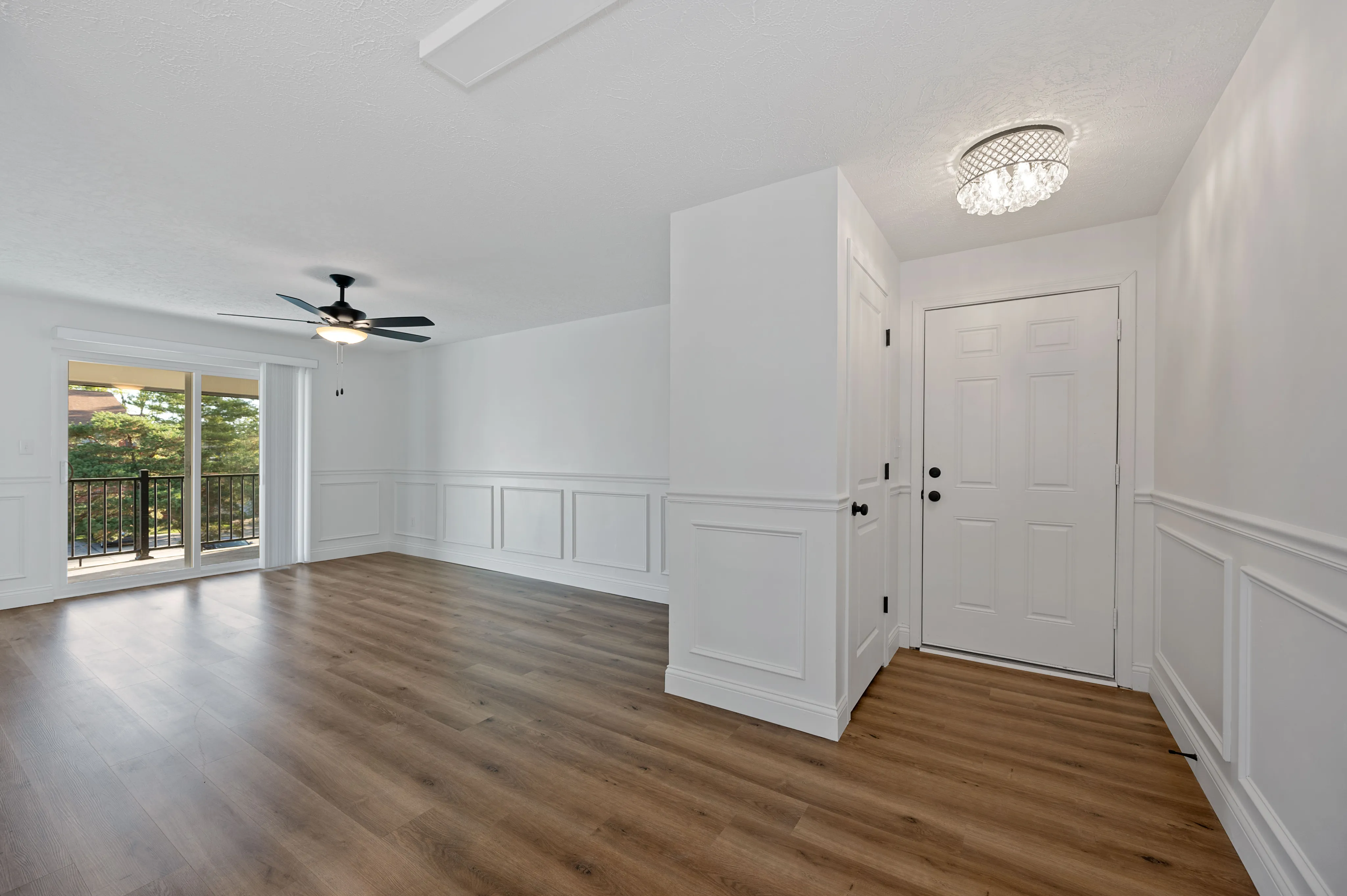 Bright, airy living space with elegant wood flooring, ceiling fan, and sliding glass doors leading to a balcony with lush views.