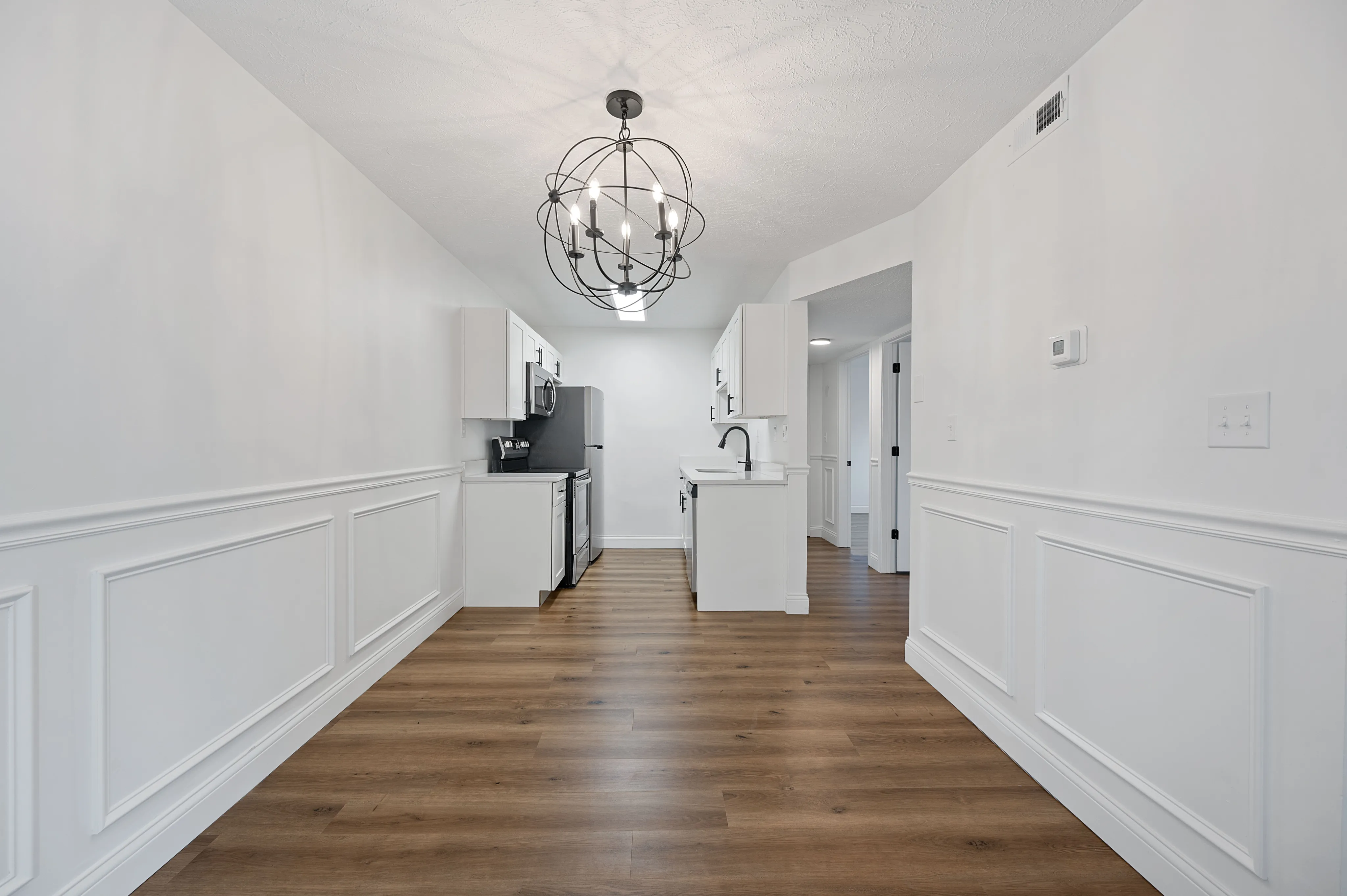 Sleek, modern kitchen with chic lighting, elegant white cabinetry, and sophisticated wood flooring.