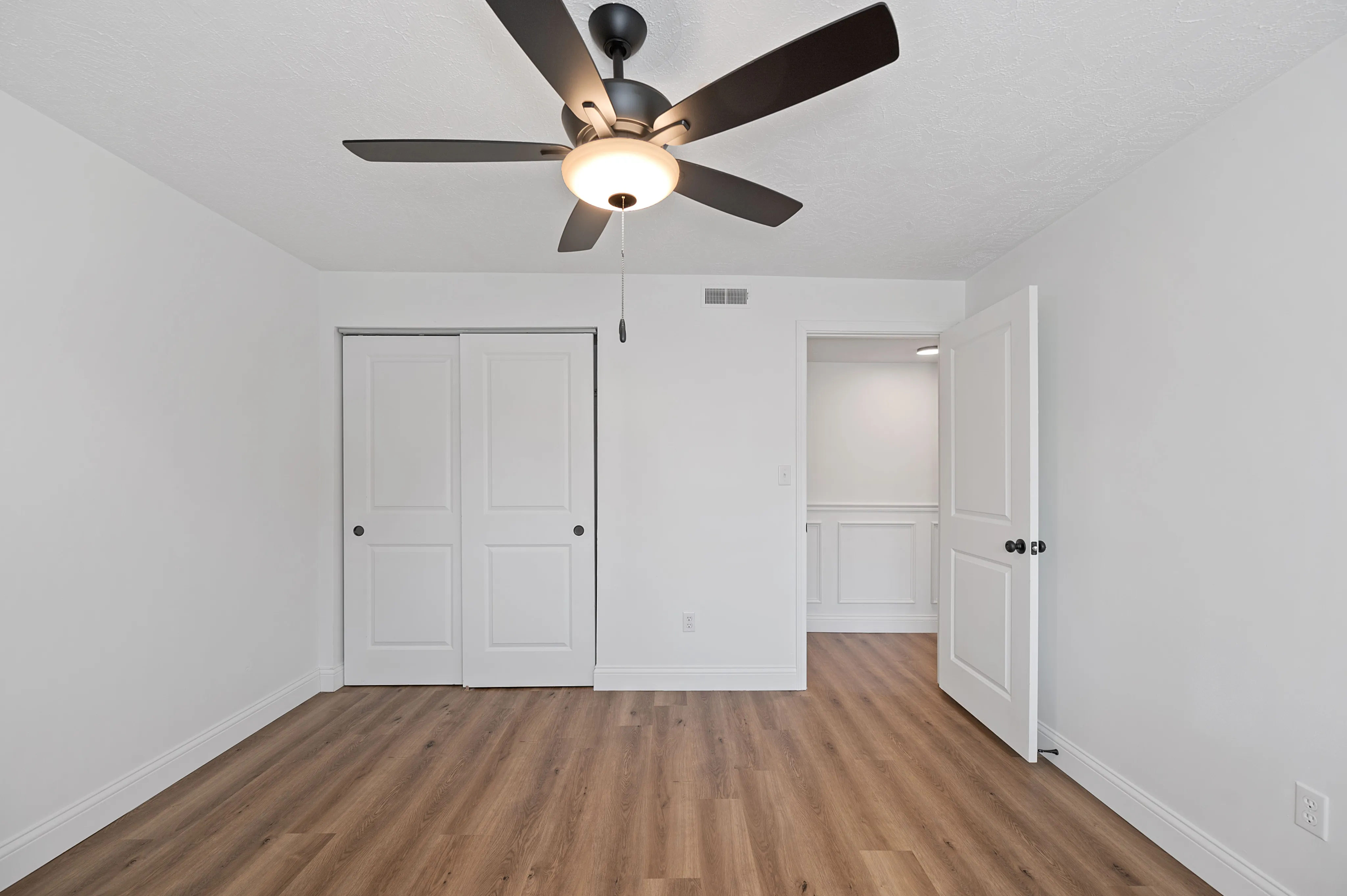 Bright and modern bedroom with elegant ceiling fan and sleek wooden flooring, featuring double closet doors for ample storage.
