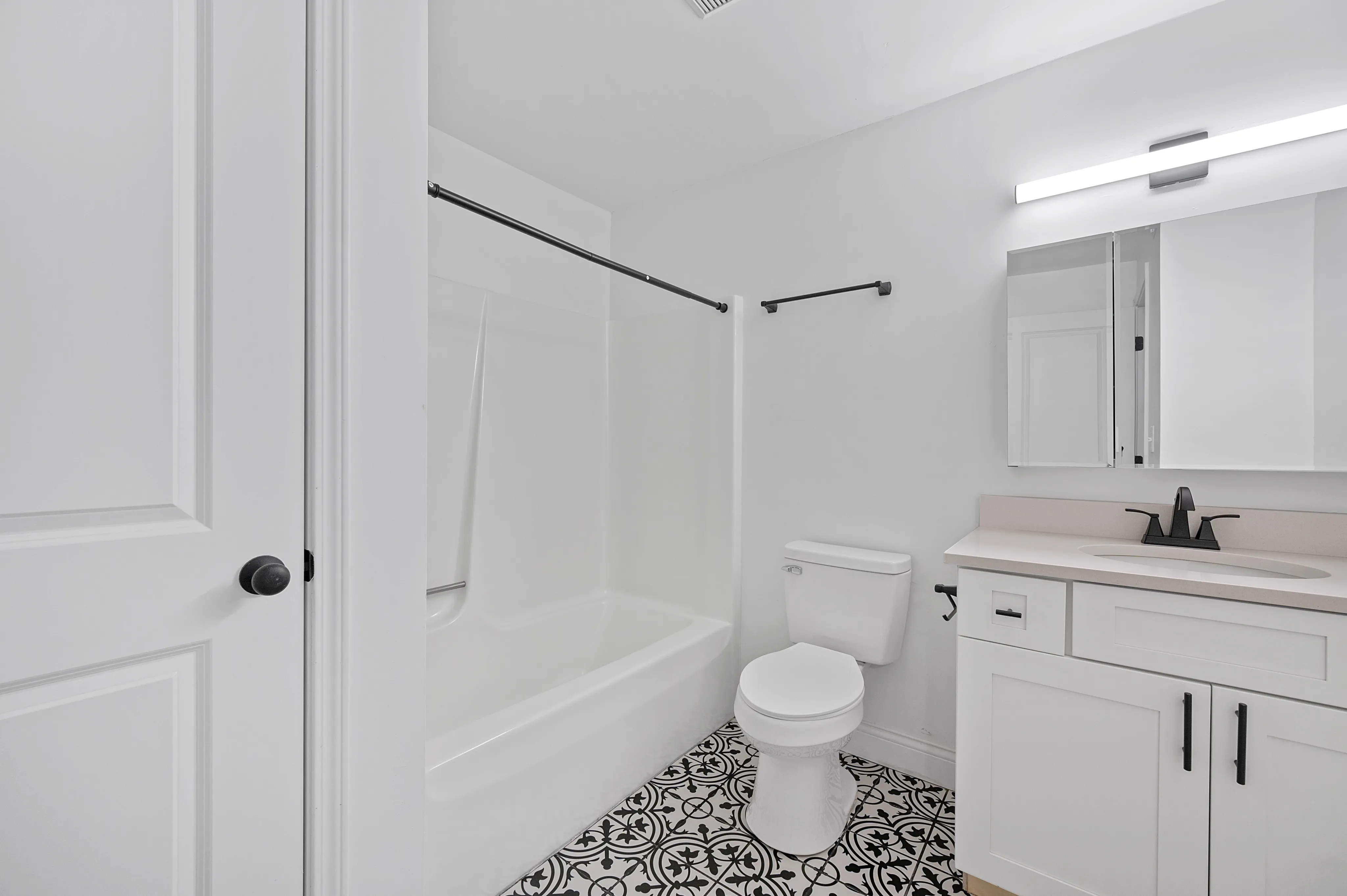 Modern bathroom with elegant monochrome tile flooring, a sleek white bathtub, and a stylish vanity with ample lighting.