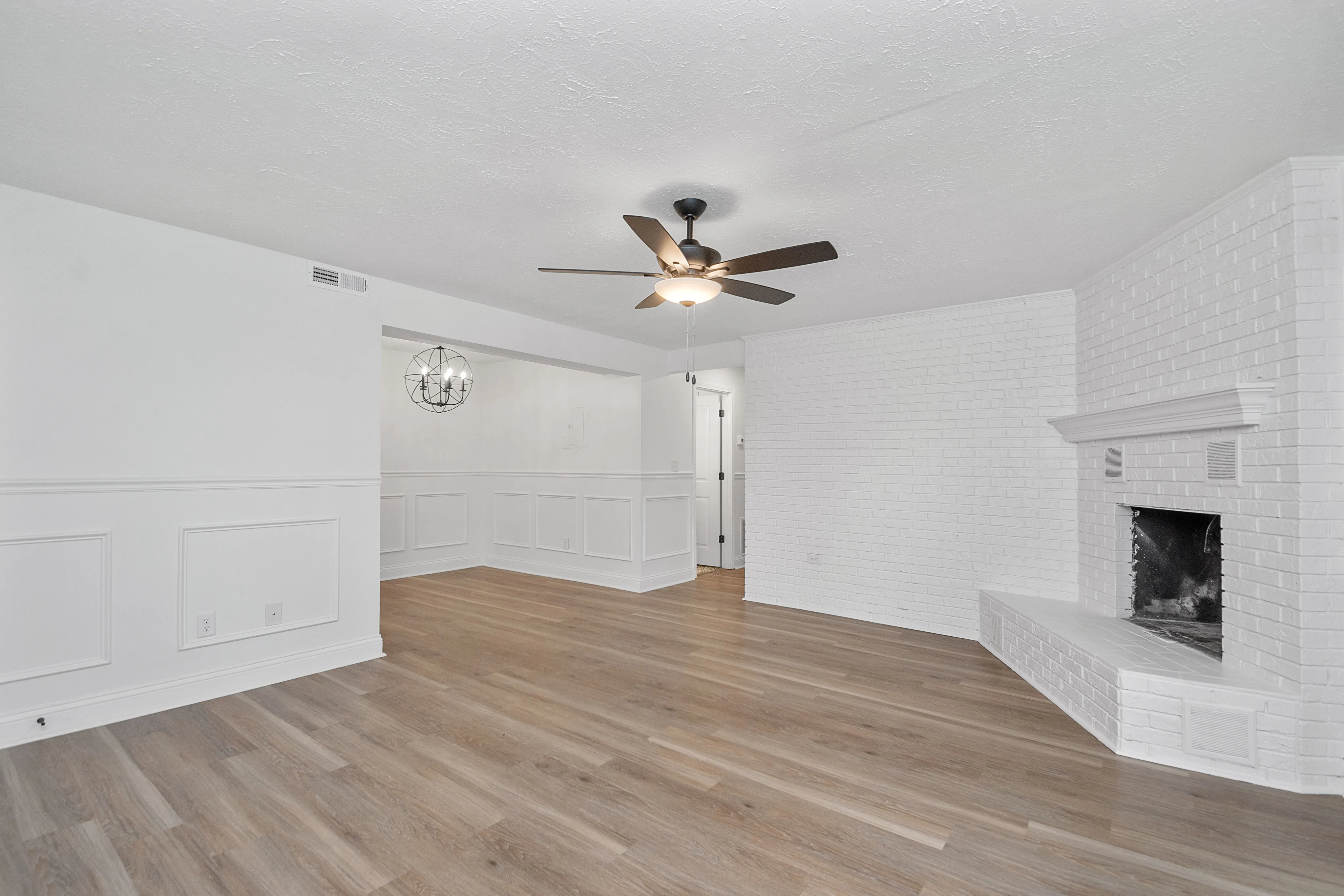 Charming living room with elegant wood flooring, a classic white brick fireplace, and a modern ceiling fan above.