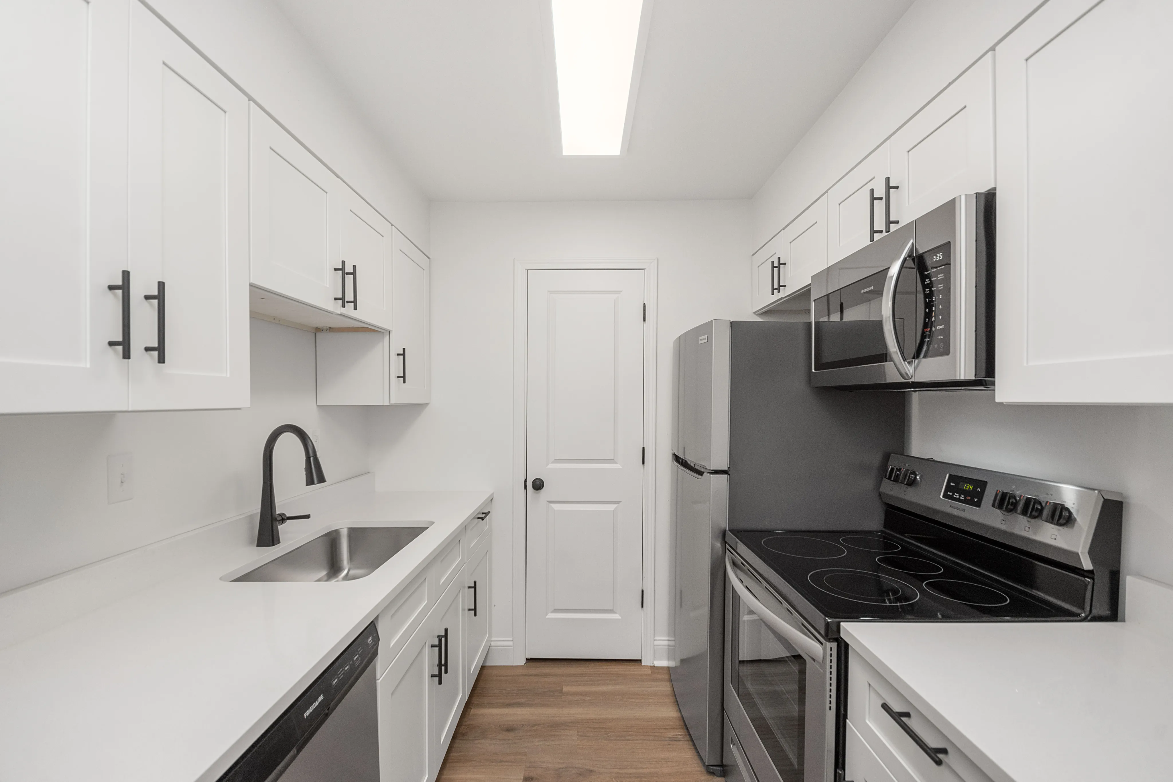 Modern white kitchen with sleek cabinetry, stainless steel appliances, and hardwood flooring.