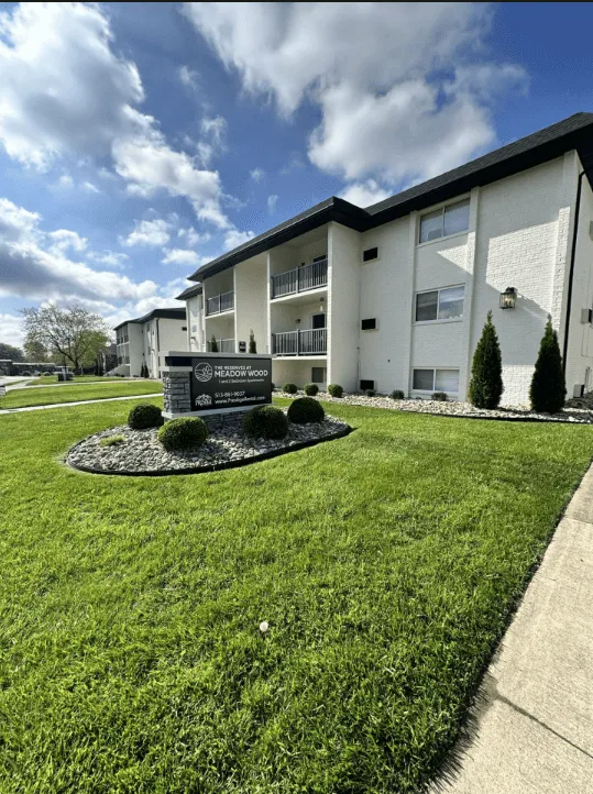 Charming apartment building with lush green lawns and well-maintained landscaping under a bright blue sky.