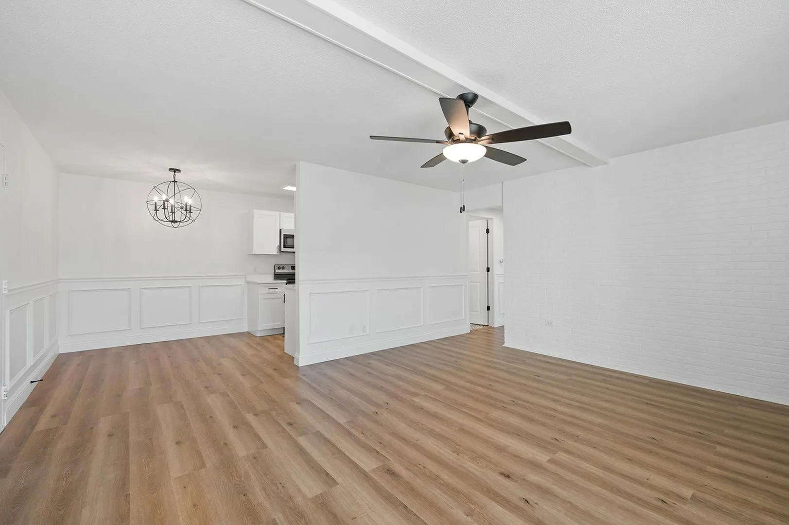 Bright and modern open-concept living area with hardwood flooring, a sleek ceiling fan, and elegant panel molding, connected to a stylish white kitchen with contemporary lighting.