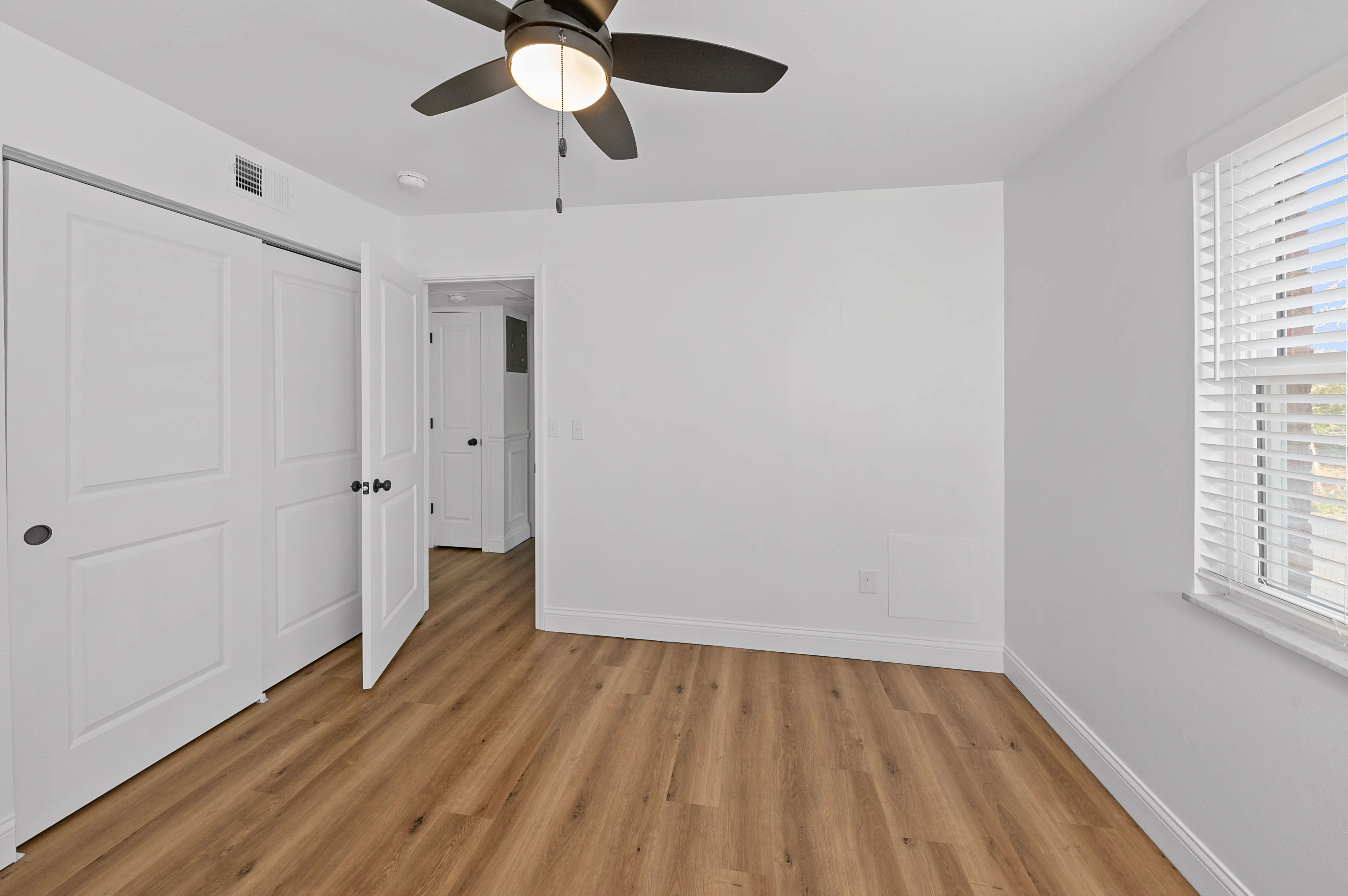Bright bedroom featuring elegant wood flooring, modern ceiling fan, and ample natural light from large window.