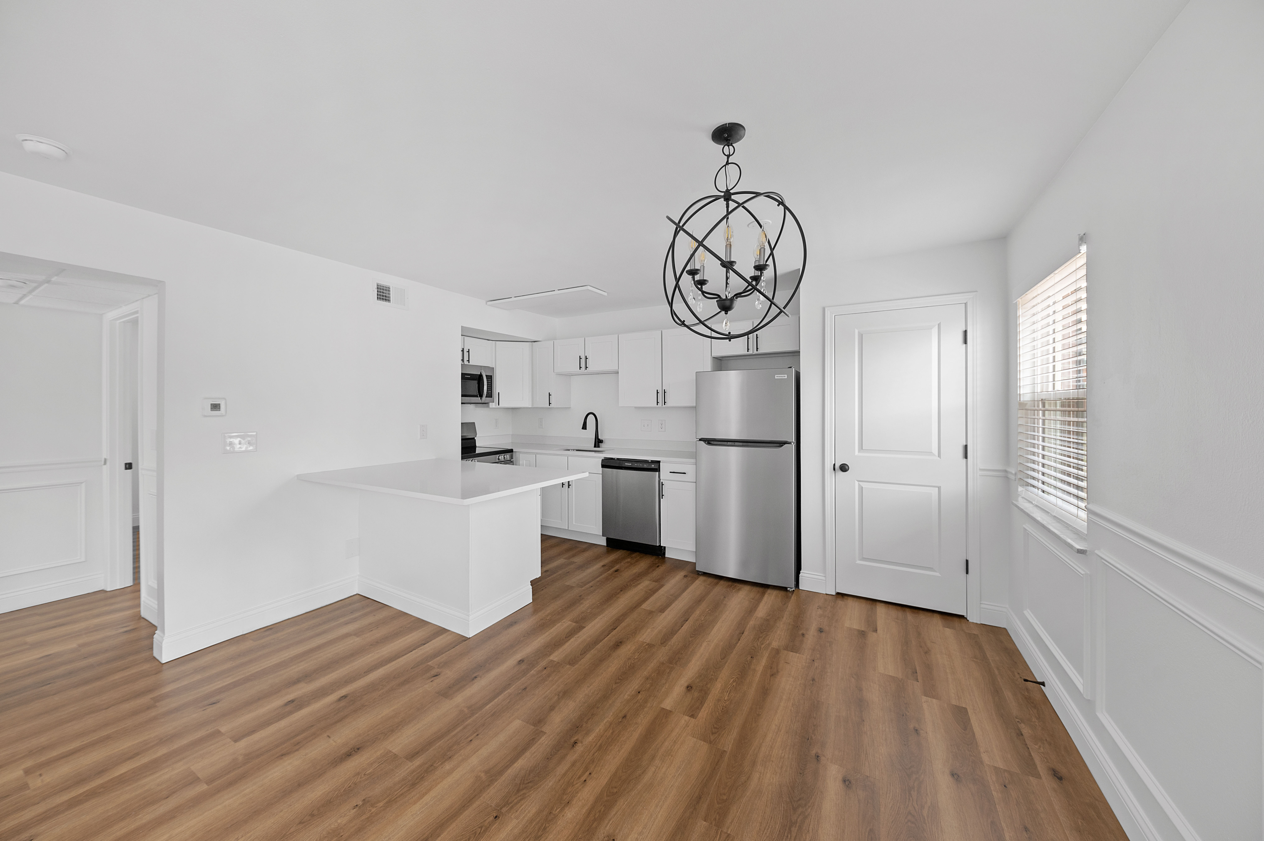 Modern kitchen with sleek white cabinetry, stainless steel appliances, and elegant pendant lighting, set in an open space with beautiful wooden floors.
