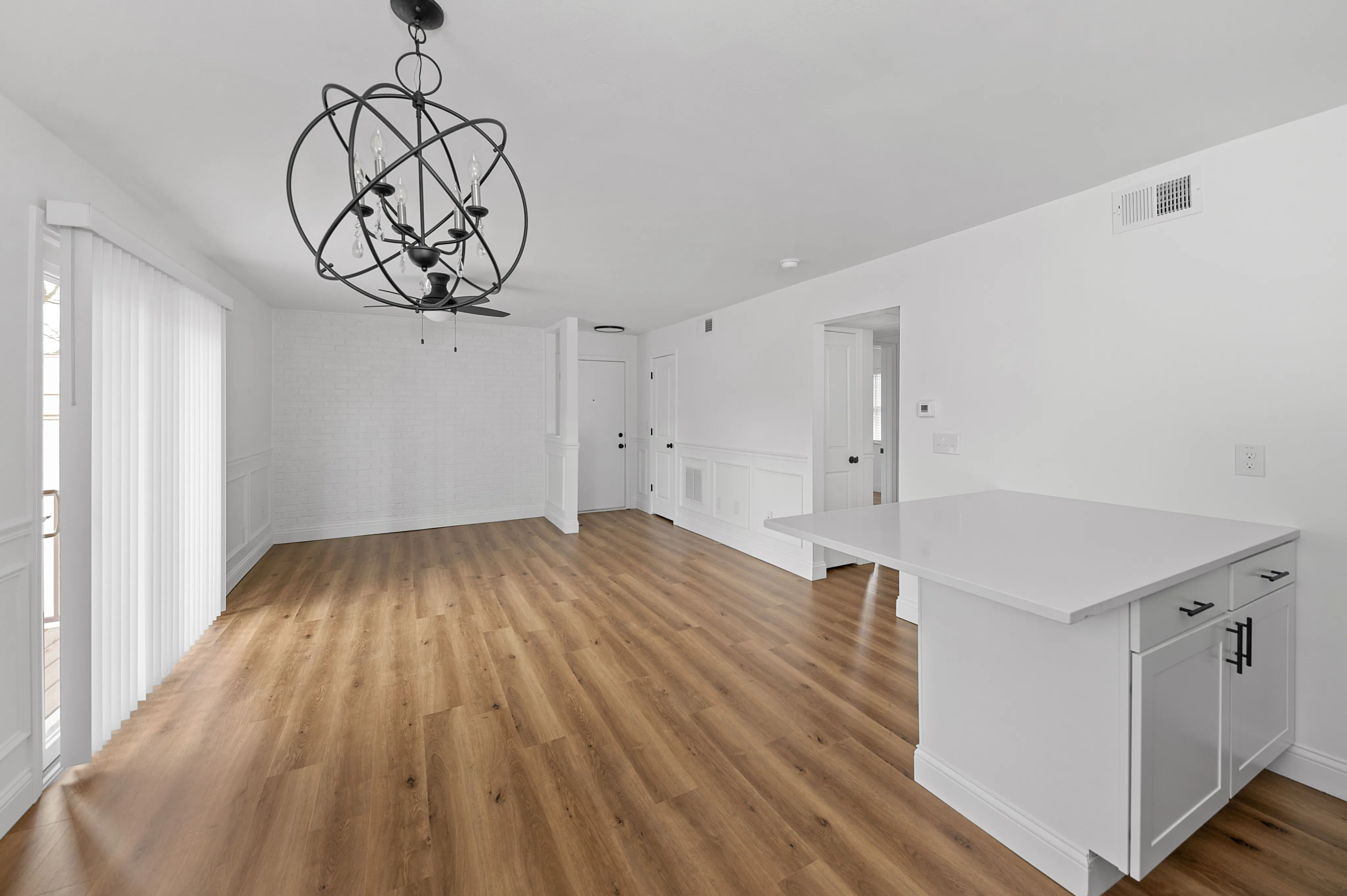 Bright open-concept living area with elegant modern chandelier, sleek white kitchen island, and rich wood flooring.