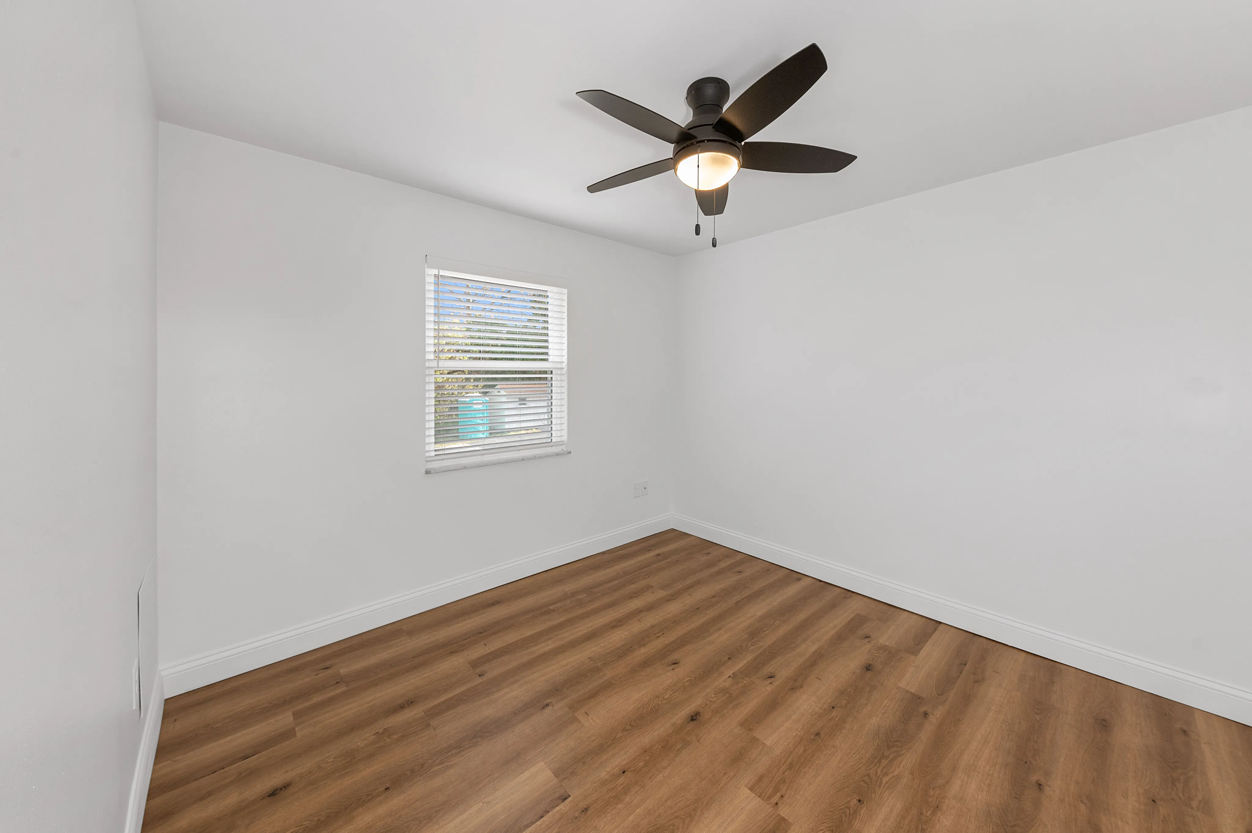 Bright, spacious bedroom with elegant wooden flooring, large window, and modern ceiling fan, perfect for cozy living.