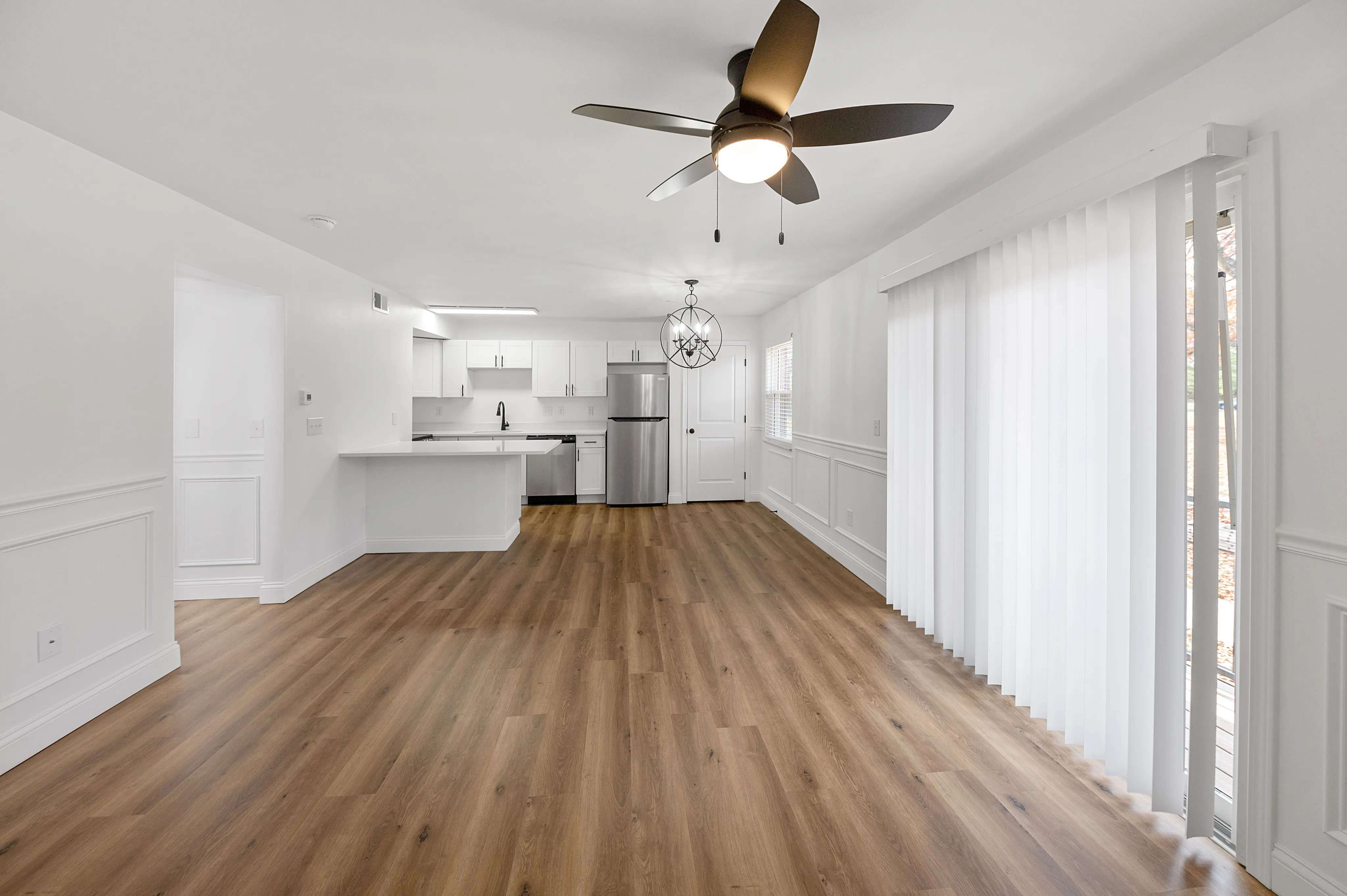 Modern open-concept living area with stylish ceiling fan, hardwood floors, and sleek kitchen featuring stainless steel appliances.
