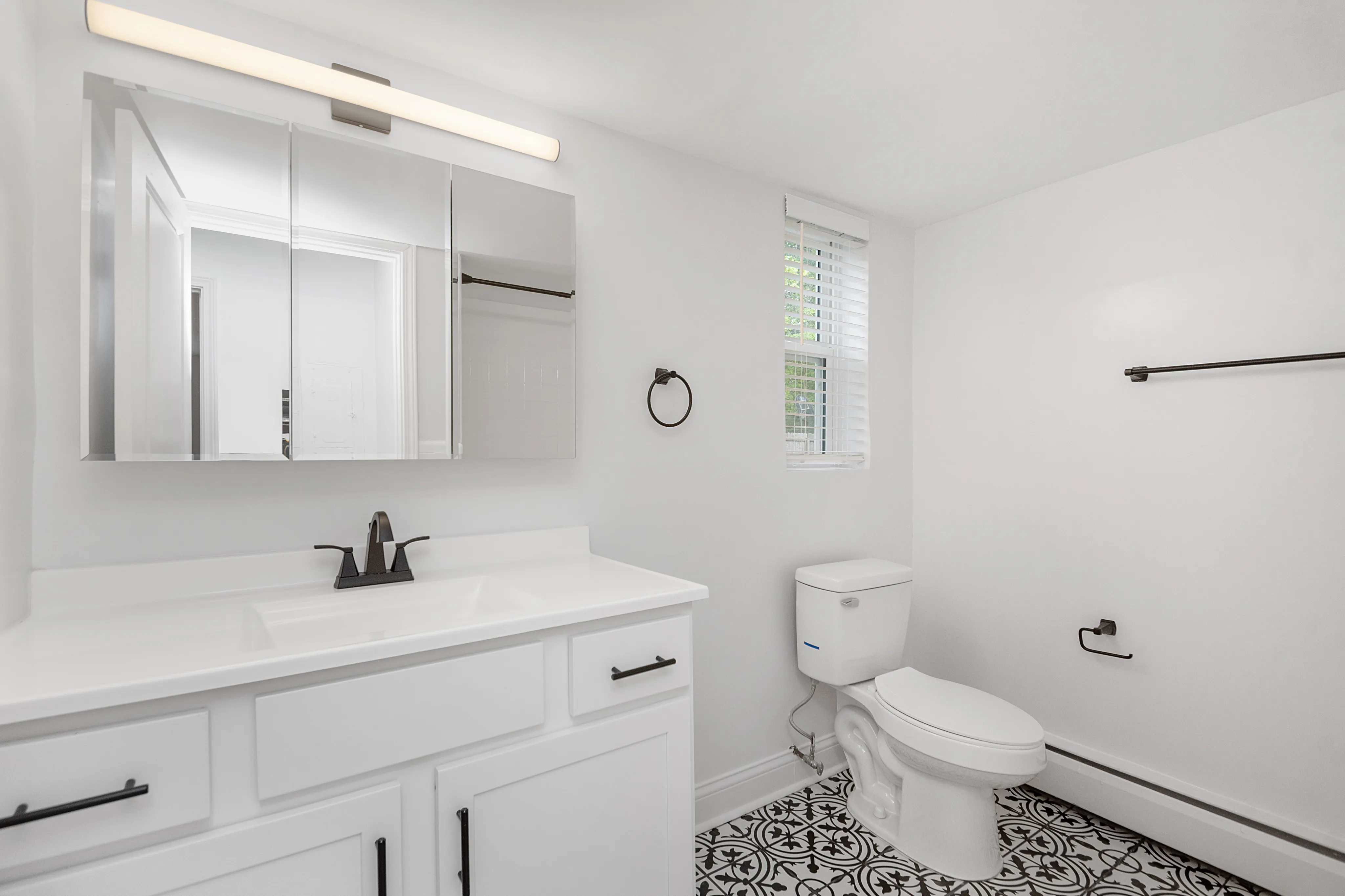 Bright, contemporary bathroom with sleek mirror cabinets, elegant fixtures, and patterned floor tiles.