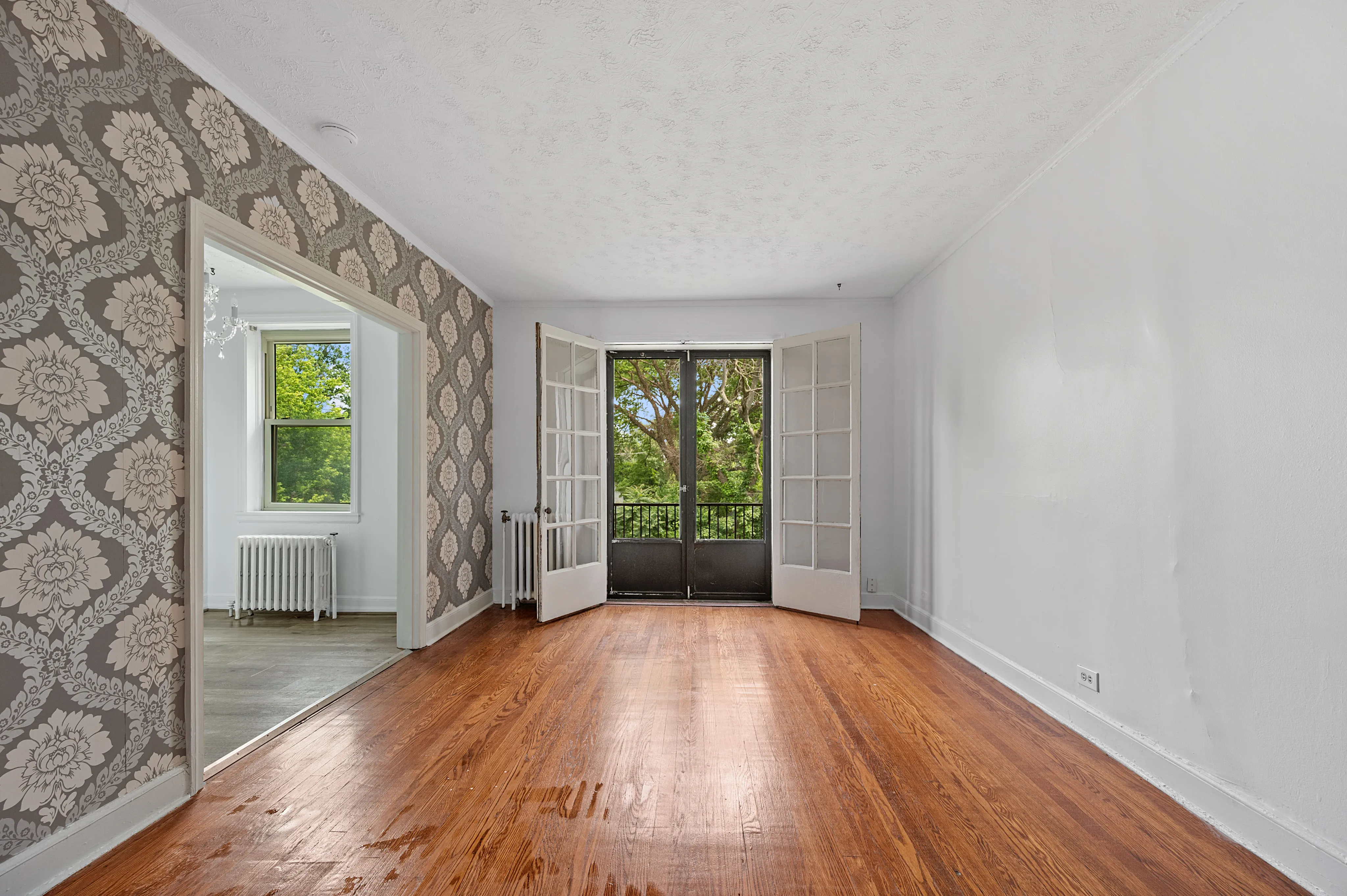 Inviting living space with elegant patterned wallpaper, rich hardwood floors, and French doors opening to lush greenery.
