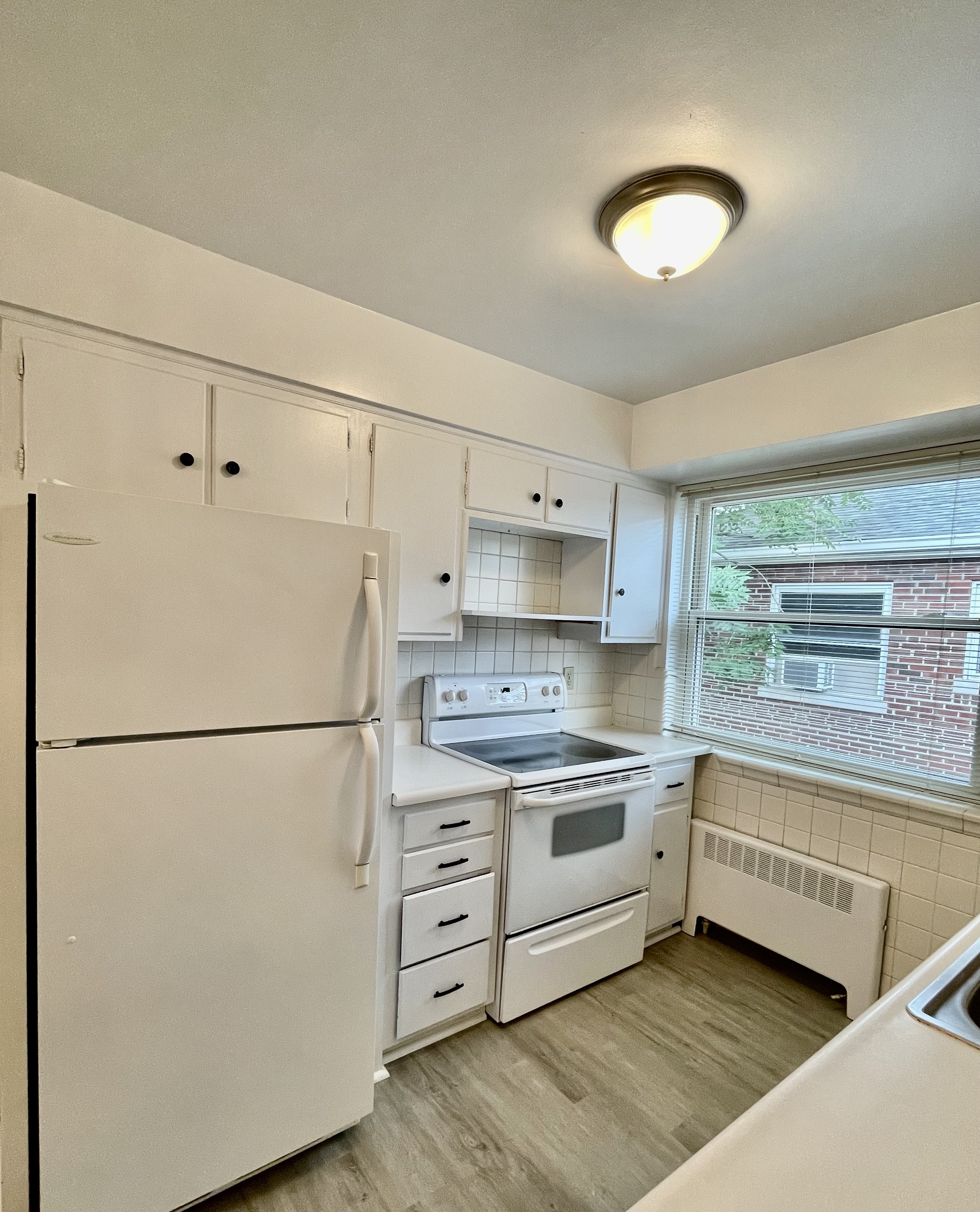 Bright and charming kitchen with white cabinetry, modern appliances, and large window offering natural light.