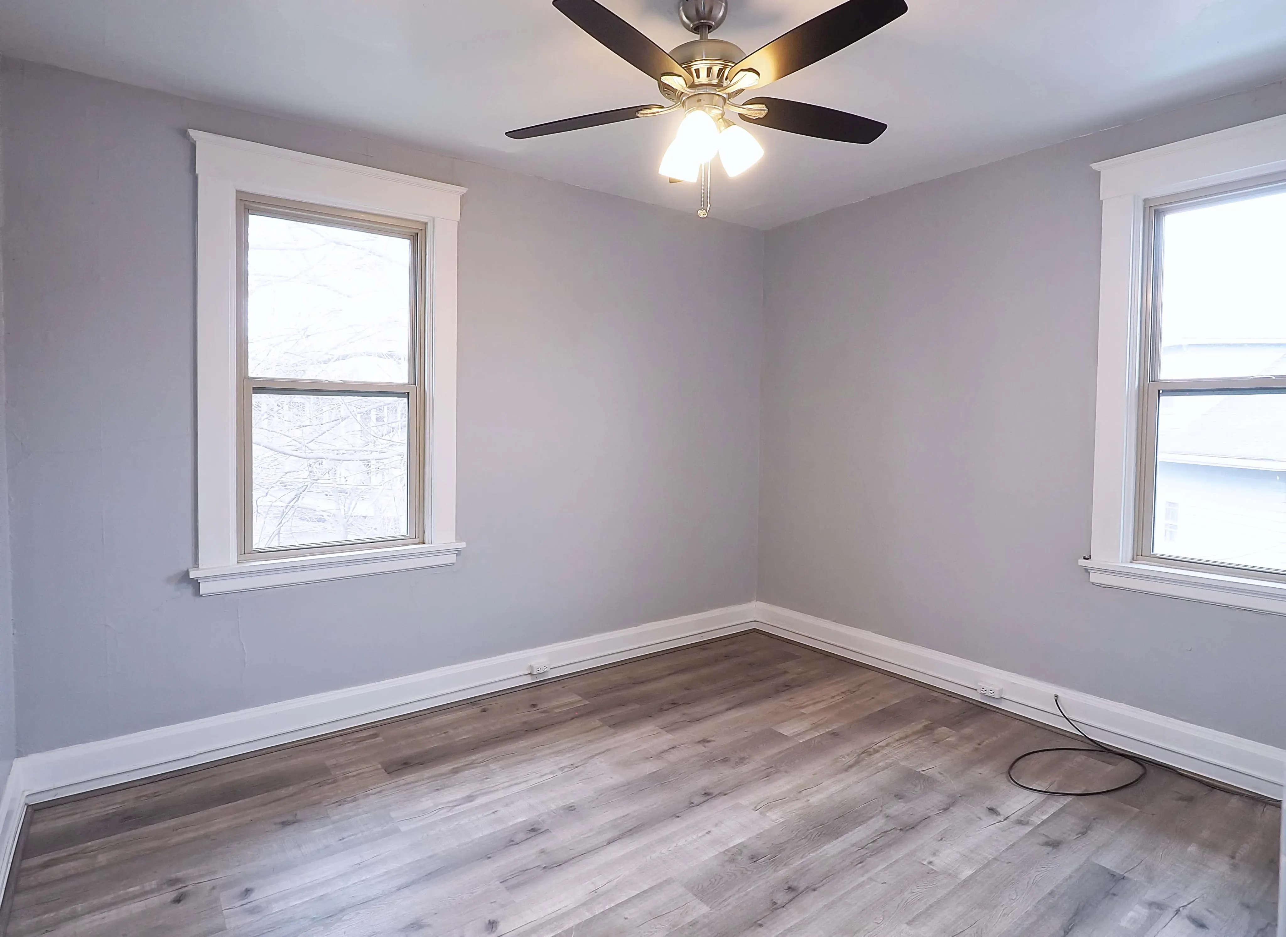 Bright and airy room with sleek wooden flooring, large windows, and a modern ceiling fan.